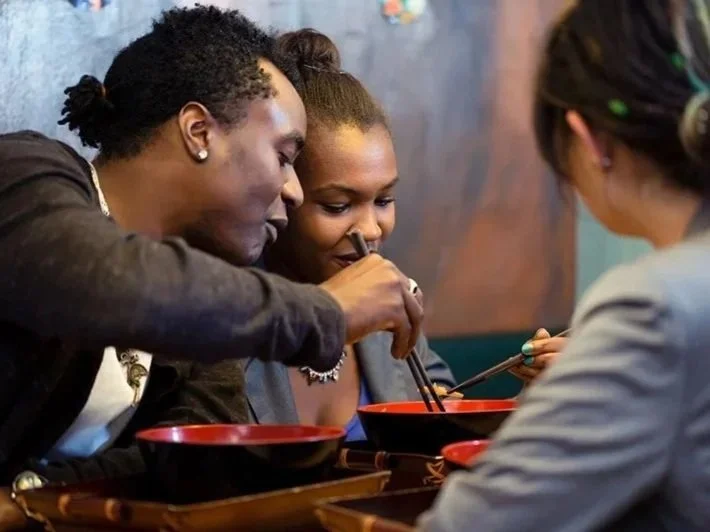 Three people are sitting at a table and eating with chopsticks, sharing a meal in a restaurant.
