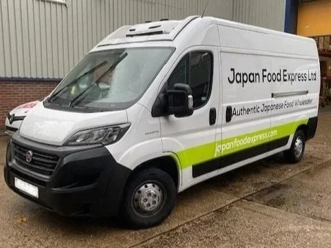 White delivery van with green stripe, labeled 'Japan Food Express Ltd' with the tagline 'Authentic Japanese Food Wholesale' and website 'japanfoodexpress.com' parked outdoors.