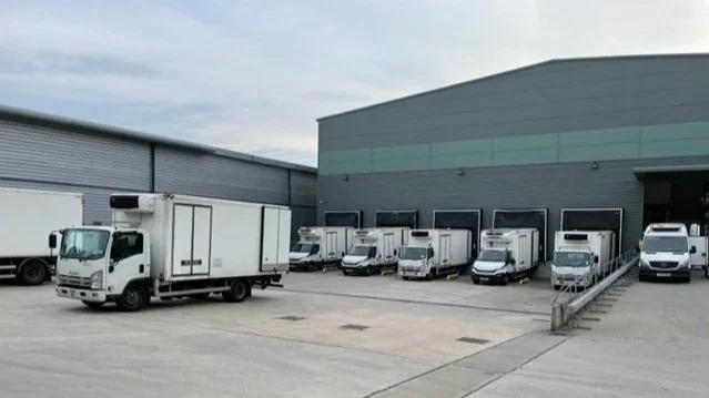 Multiple delivery trucks and vans parked outside a warehouse.