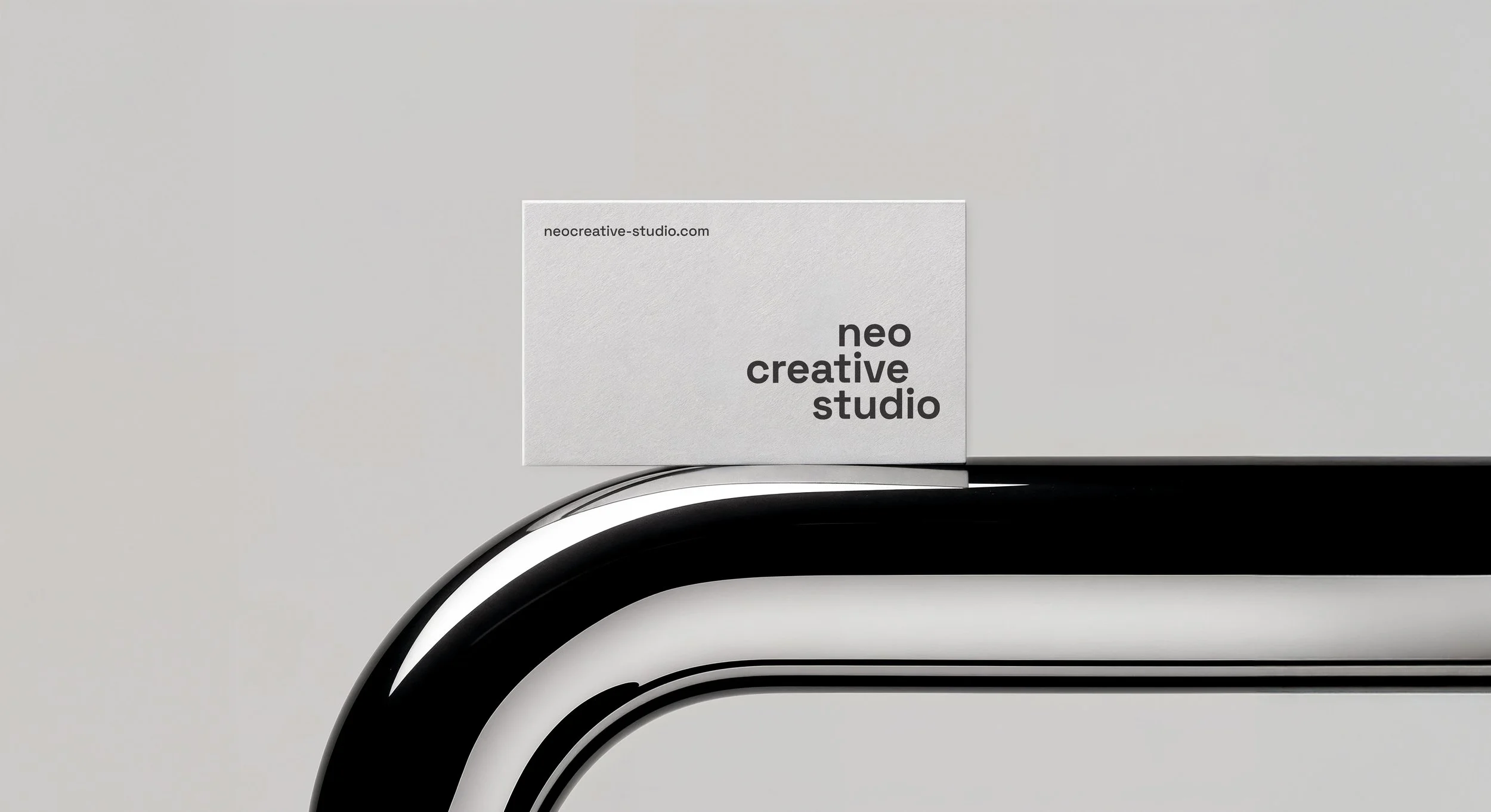 A modern, minimalist business card with the text 'neo creative studio' and the website 'neocreative-studio.com' on a white background, placed on a sleek, curved black and white object.