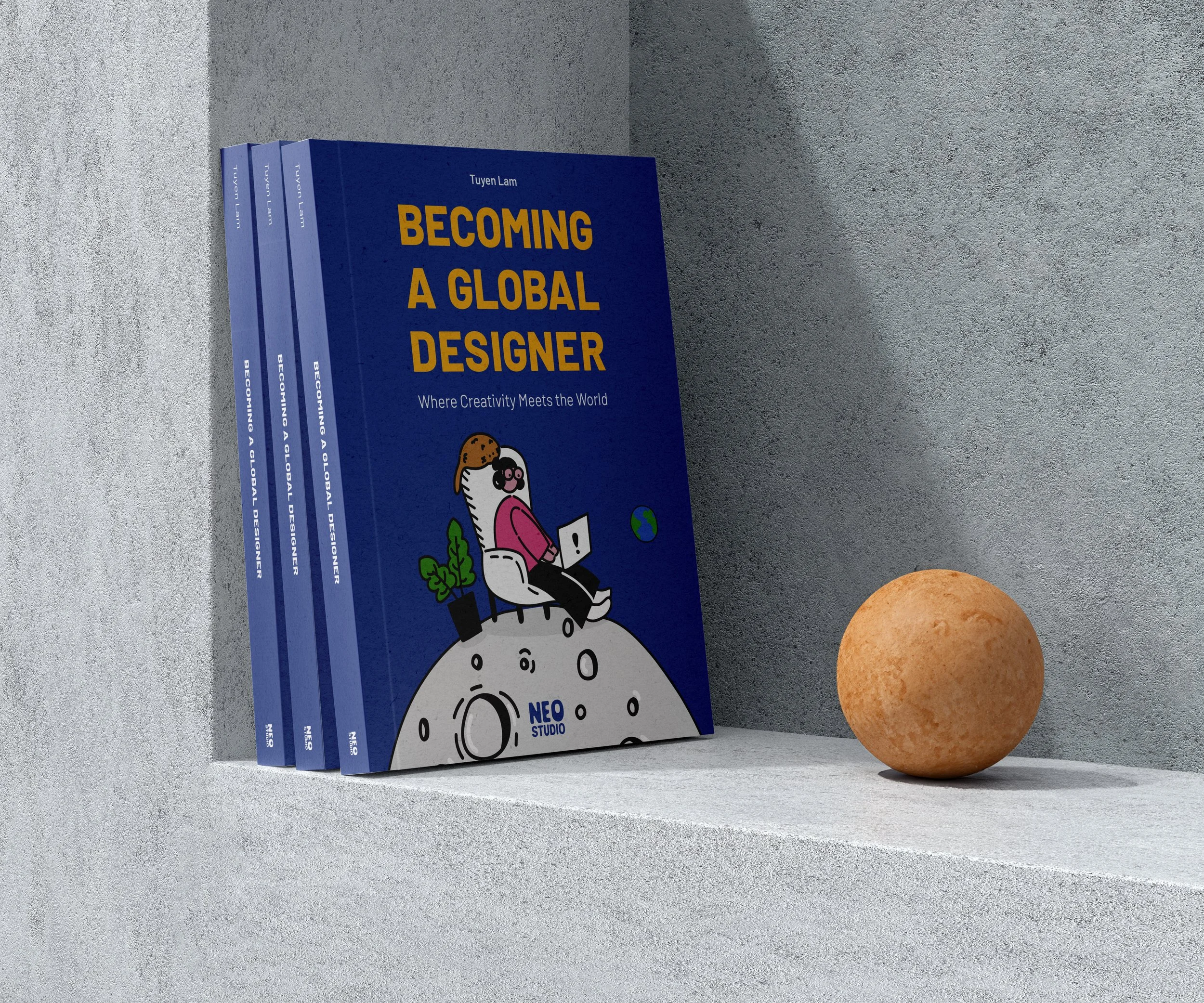 A row of blue books titled 'Becoming a Global Designer' on a gray shelf, with a cartoon character illustration on the front cover, placed next to a round, orange-brown object.