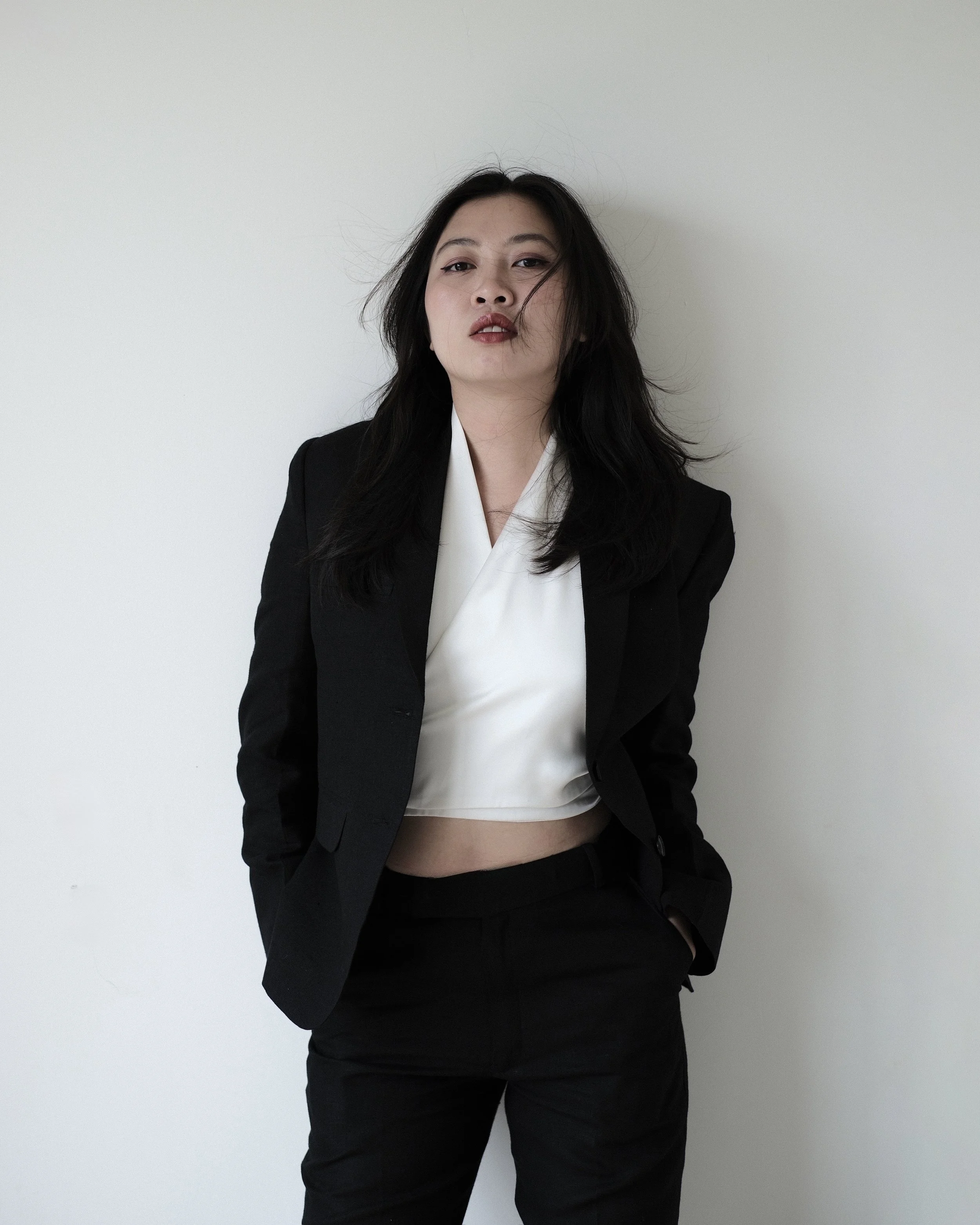 Tuyen Lam is wearing a black blazer over a white top, posing against a plain white wall.