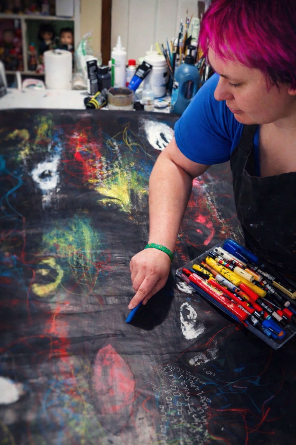 Tegan Bailey working on an abstract painting at a studio table, surrounded by art materials.