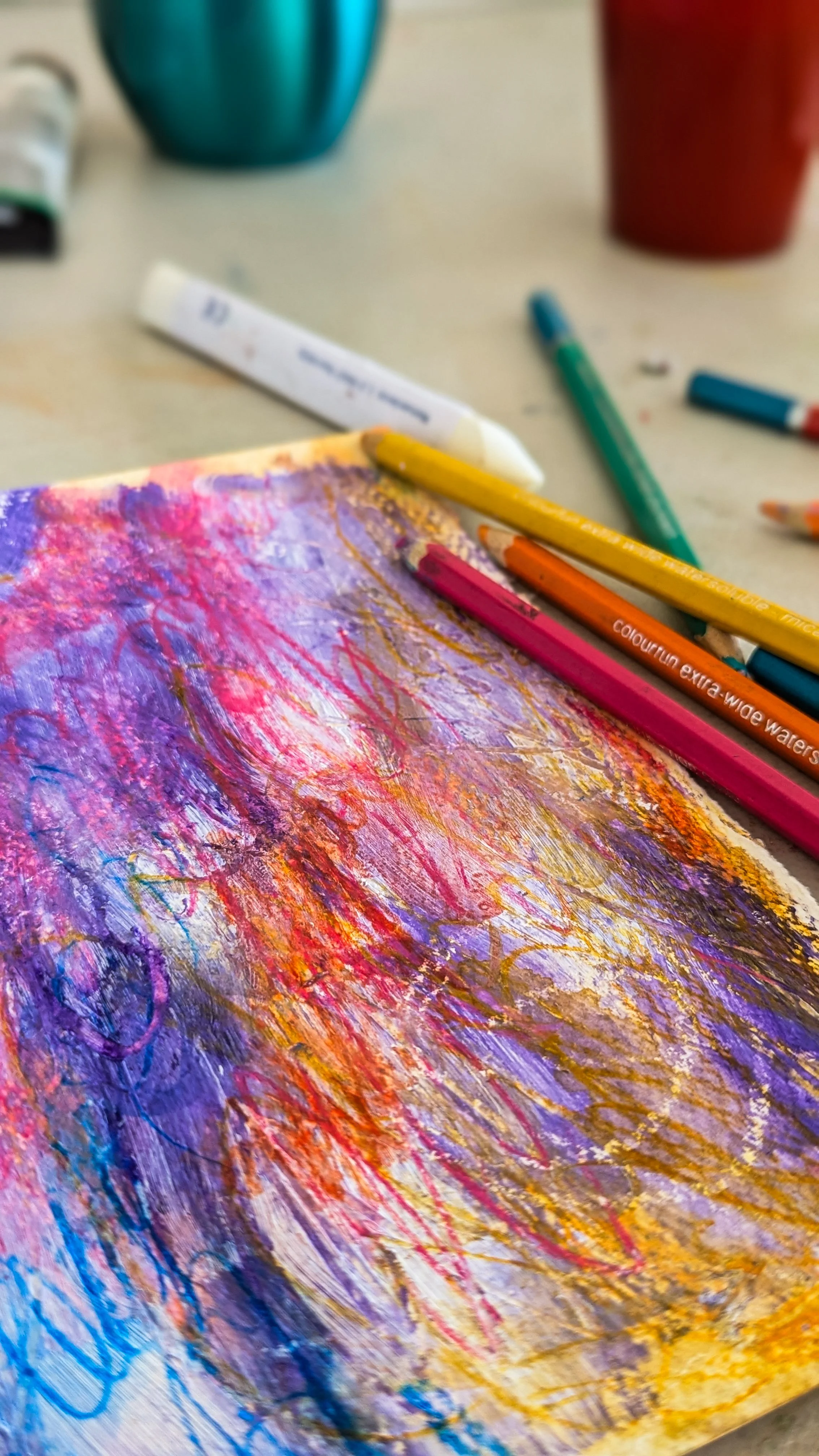 Close-up of a colorful abstract painting created with crayons and pastels on paper, with various crayons scattered around on a table.