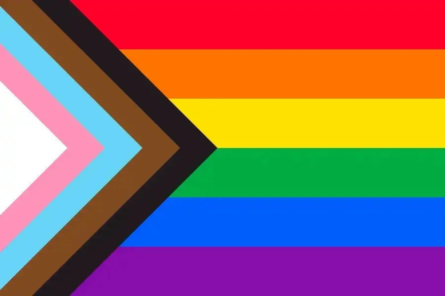 Progress Pride flag featuring rainbow stripes with a chevron of black, brown, light blue, pink and white.