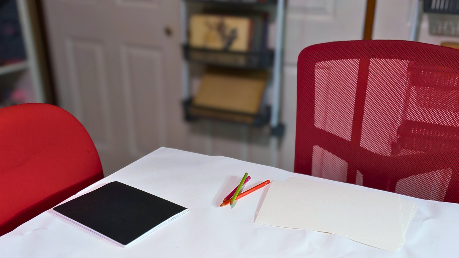 Two chairs facing each other with a table between them in a studio space, set up for a 1:1 creative arts therapy session with paper and pencils available.