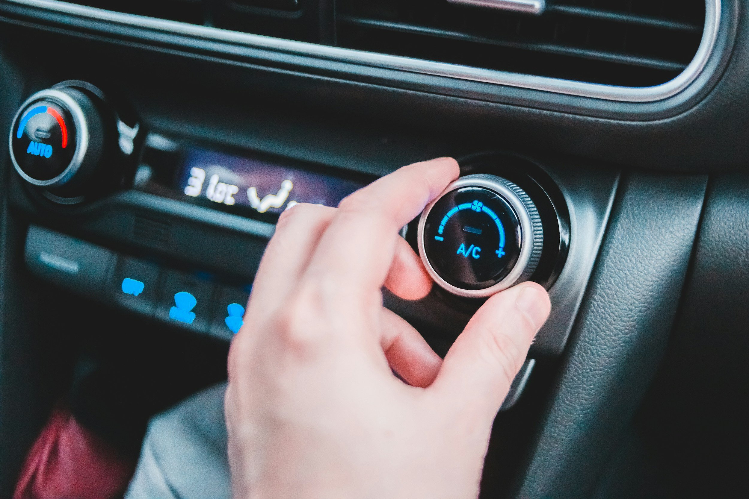 A person's hand adjusting the temperature control knob on a car's climate control system.