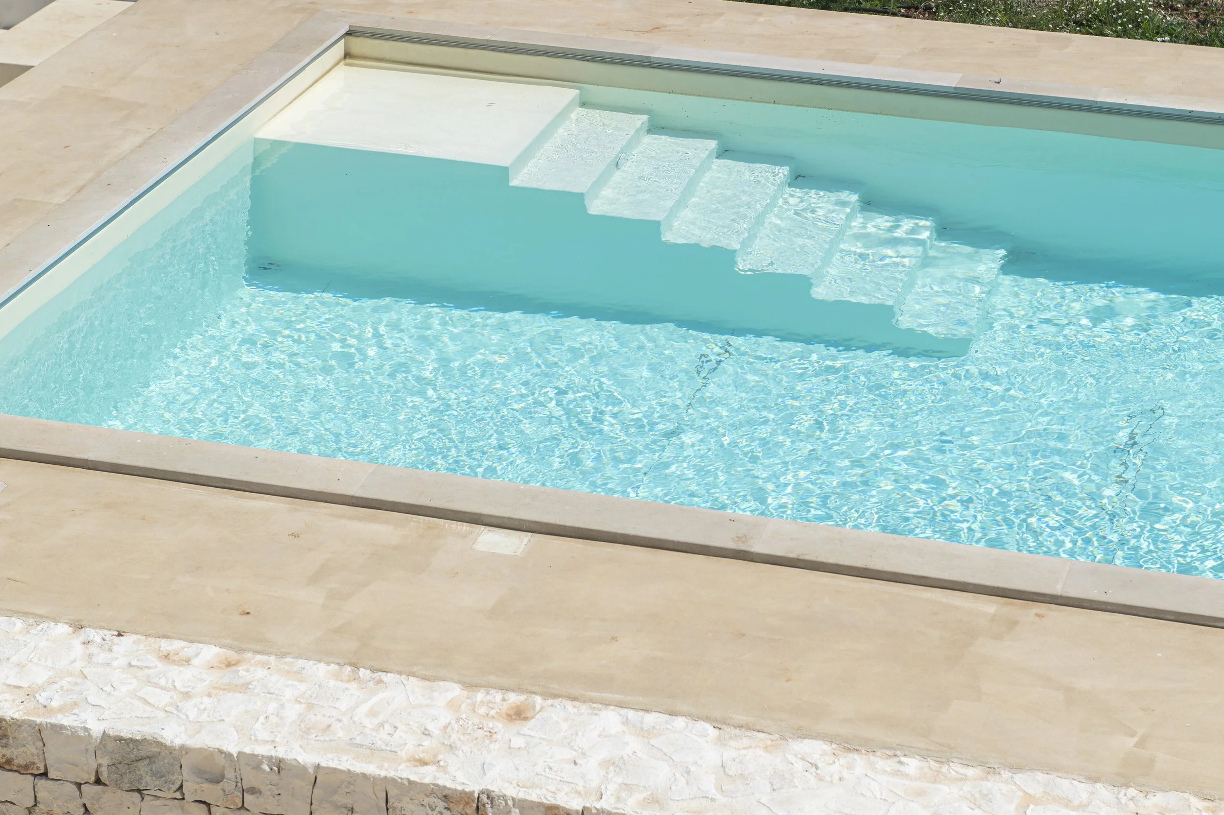 Crystal clear swimming pool with built-in stairs, surrounded by beige tile flooring.