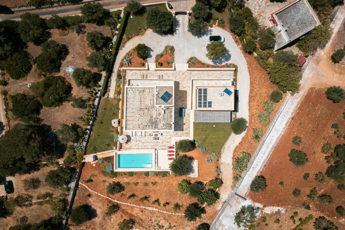 An aerial view of a modern house with a swimming pool and surrounding yard, trees, and pathways.