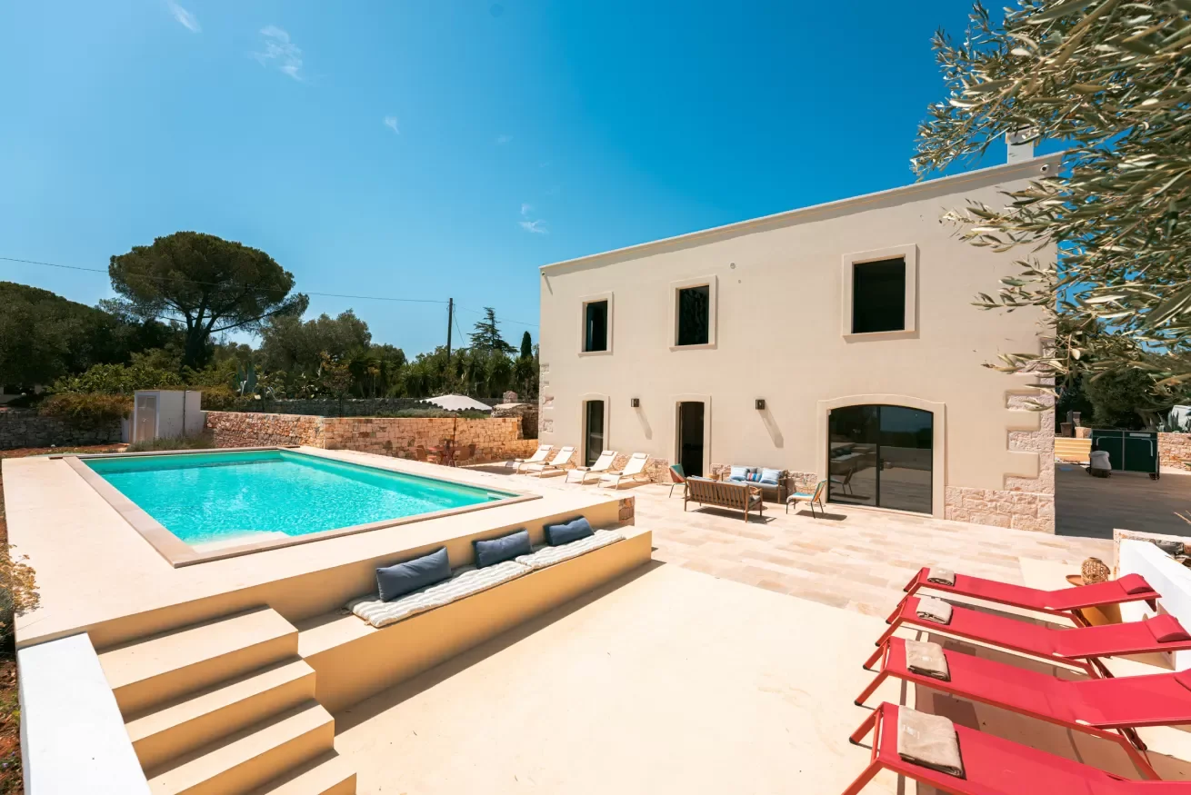 Modern house with a swimming pool in the backyard, surrounded by lounge chairs, a sofa set, and outdoor seating on a sunny day.
