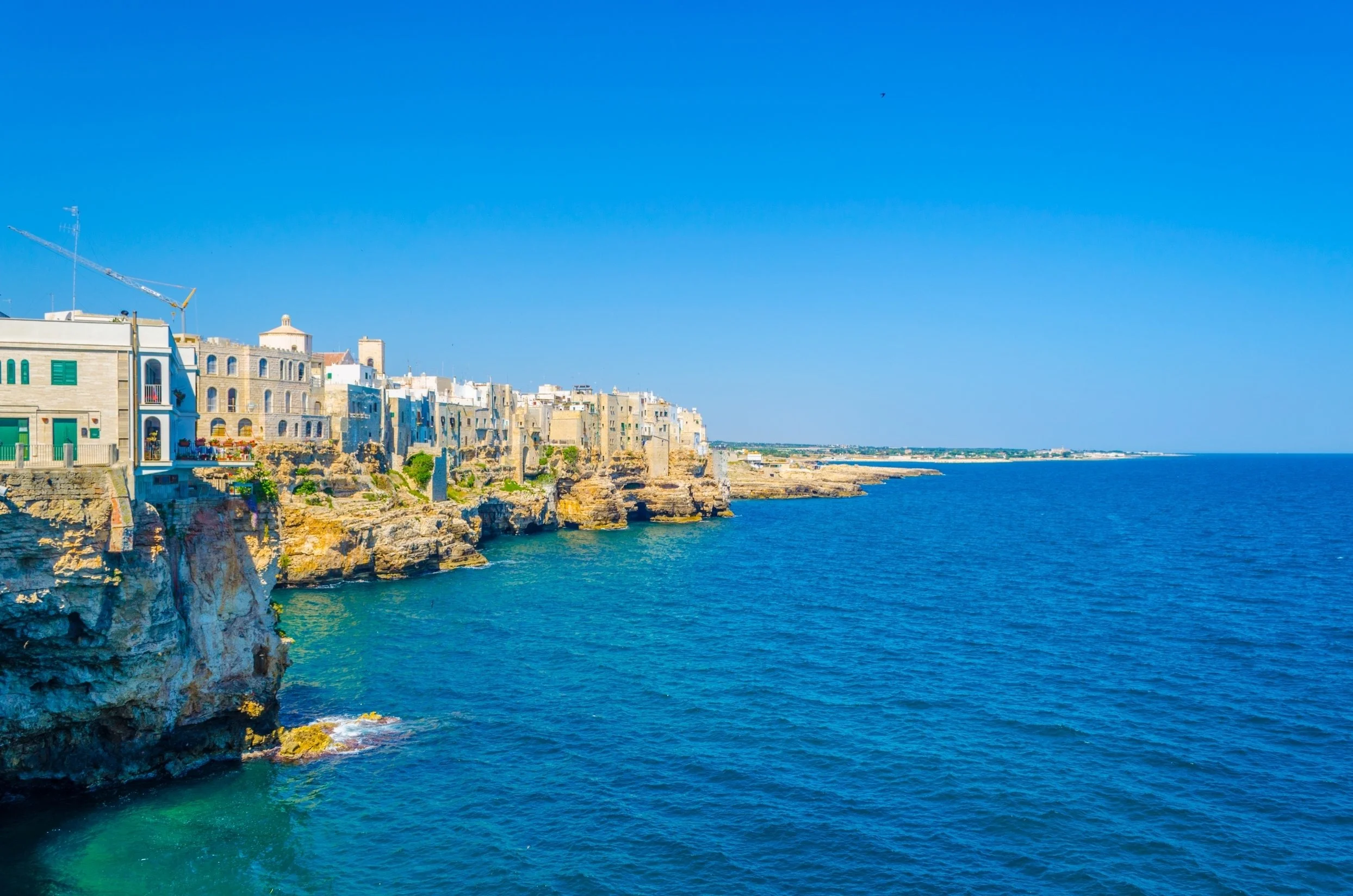 Cliffs along a coastline with colorful buildings on top and the sea below, under a clear blue sky.