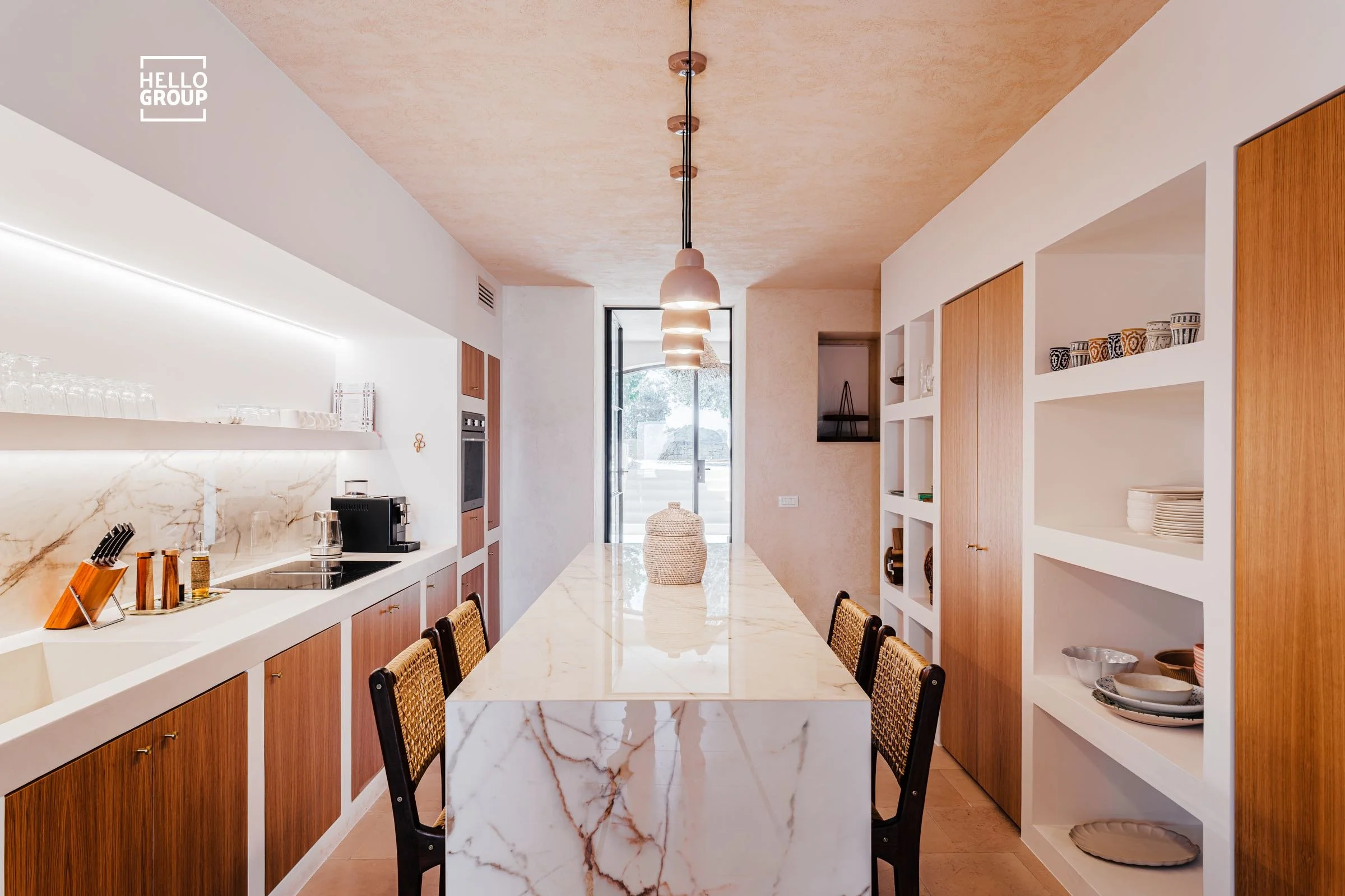 Modern kitchen with marble island and wooden cabinetry, open shelving with dishes, and natural light from a glass door.