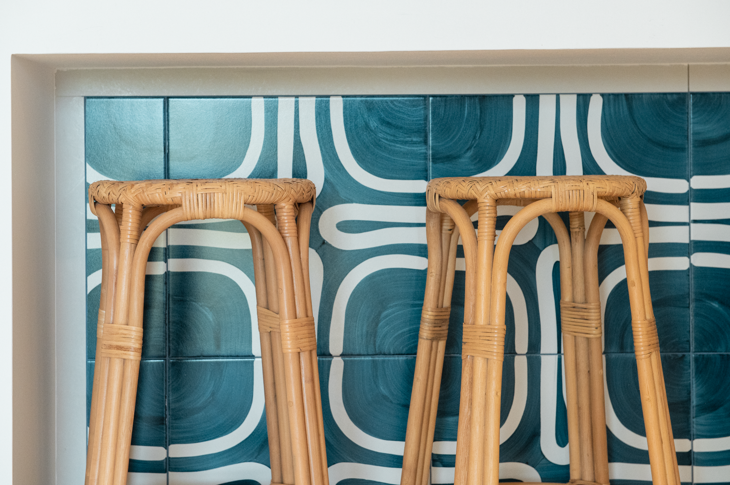 Two rattan bar stools in front of a turquoise and white patterned tiled wall.
