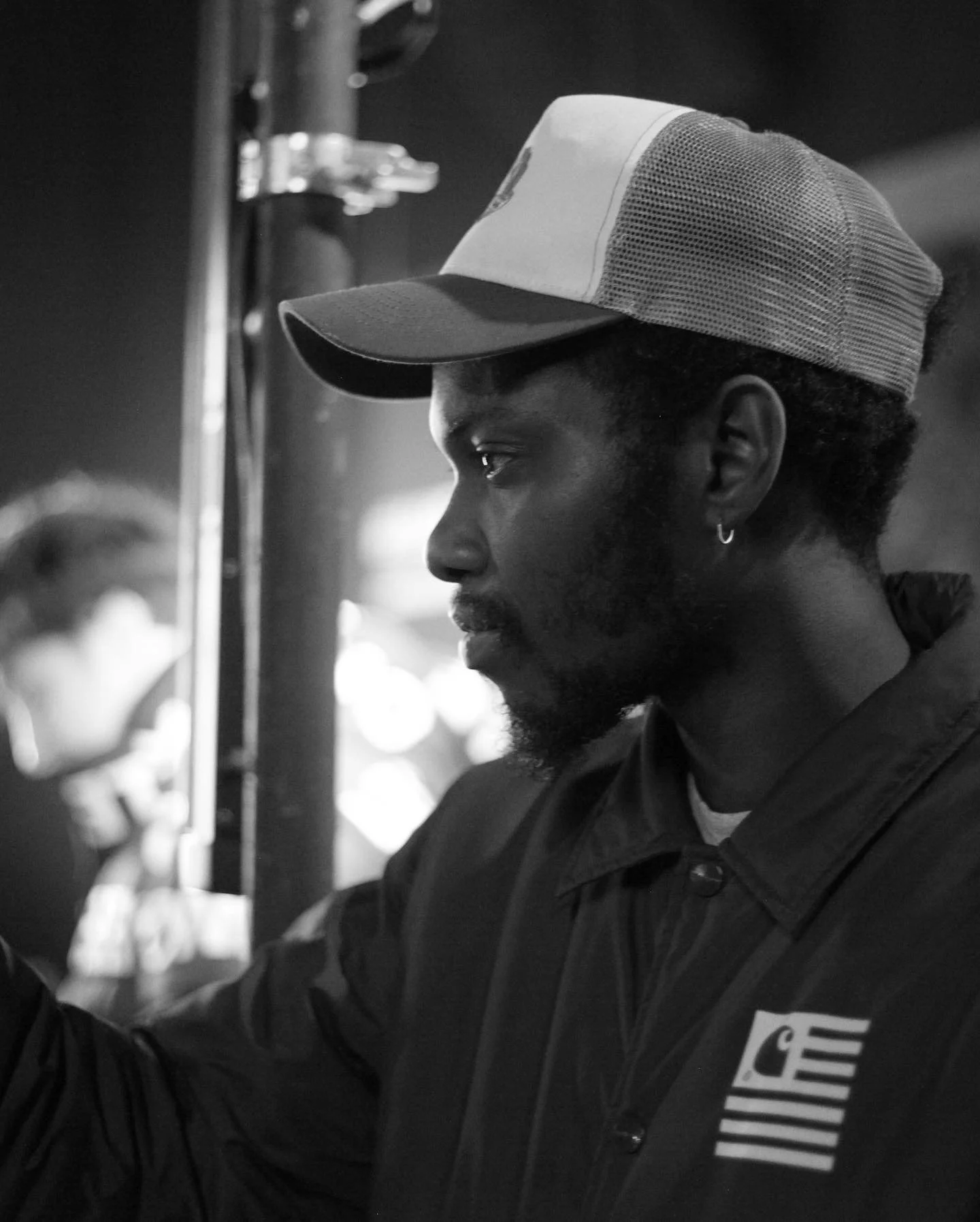A black and white side profile of a man wearing a baseball cap and a jacket with a patch of the American flag on it.