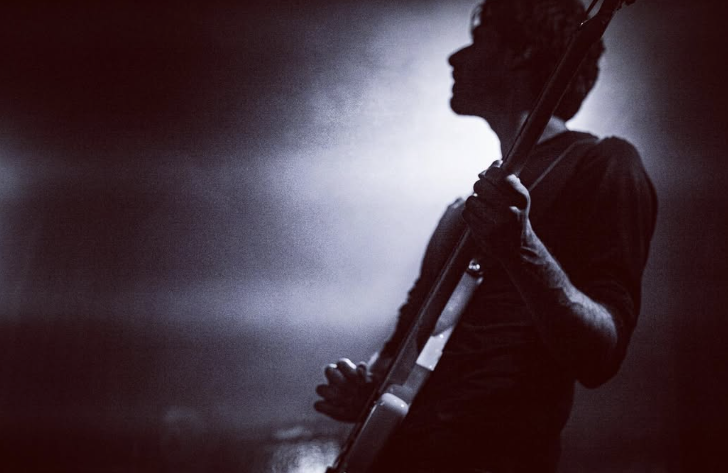 Silhouette of a person holding a guitar in a dark, smoky environment with backlighting.