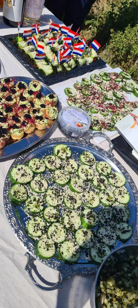 Tray of cucumber slices topped with herbs and sesame seeds, decorated for a celebration with small flags and various appetizers on a table.