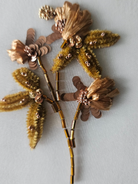 Two embroidered floral brooches with beads, sequins, and fabric embellishments on a light background.