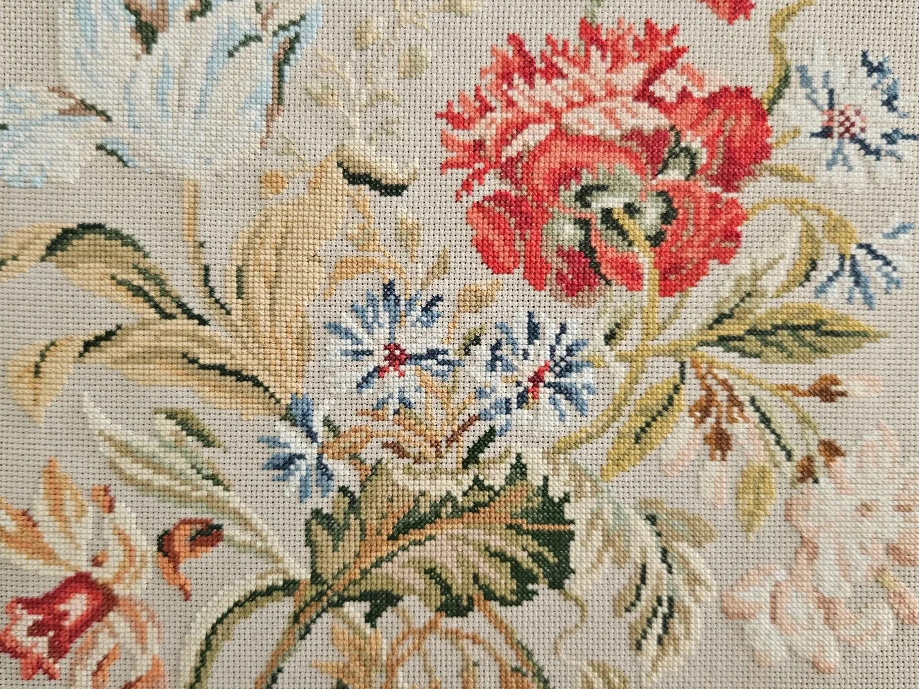 Close-up of a floral reproduction embroidery pattern with various flowers and leaves in shades of red, blue, green, and beige.