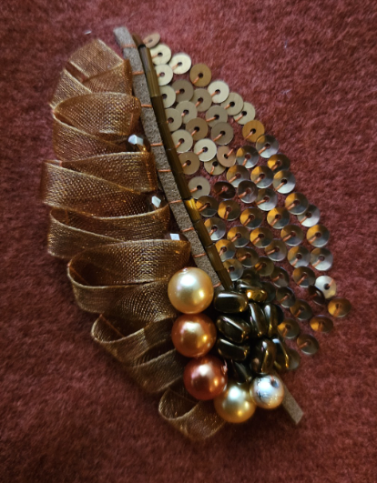 	
Decorative leaves with ribbon loops, gold beads, and pearl embellishments on a copper orange scarf.