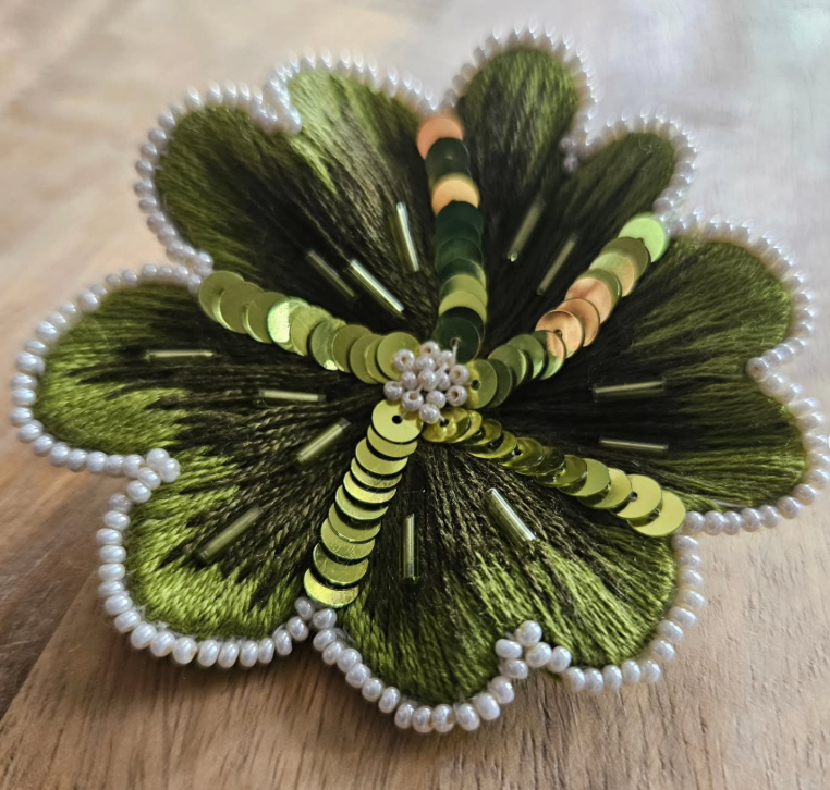 Decorative hand-embroidered shamrock made of green and yellow sequins, beads, and embroidery on fabric, with a pearl border.