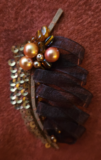 Decorative leaves with ribbon loops, gold beads, and pearl embellishments on a copper orange scarf.