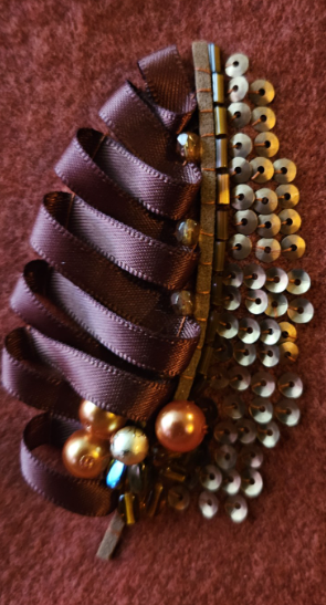 Decorative leaves with ribbon loops, gold beads, and pearl embellishments on a copper orange scarf.