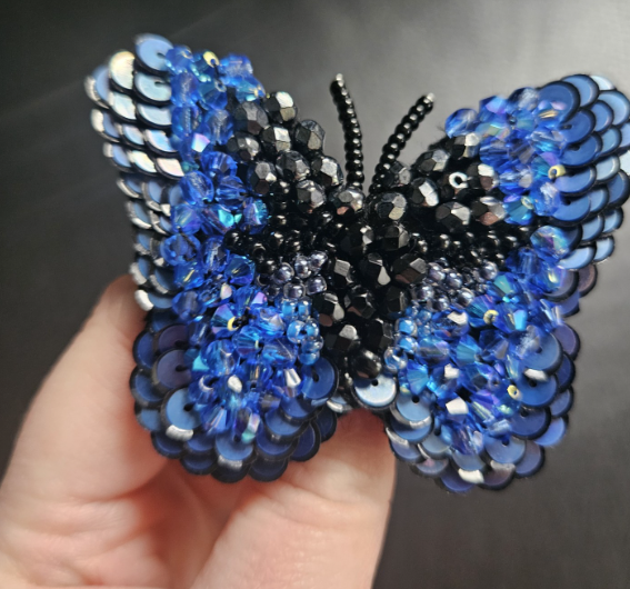 A decorative butterfly-shaped brooch decorated with blue and black sequins and beads.