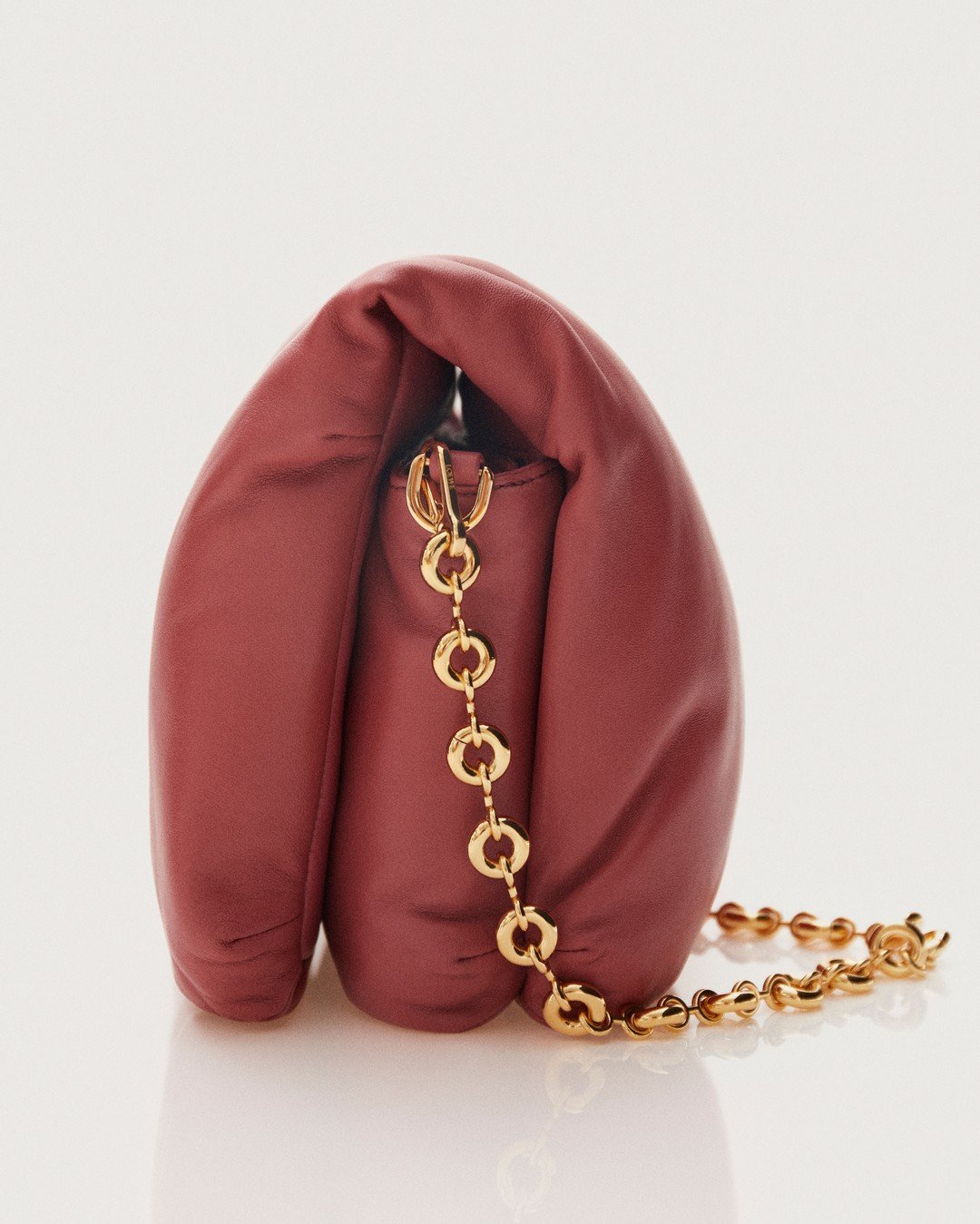 A pink leather handbag with a gold chain handle on a white surface.