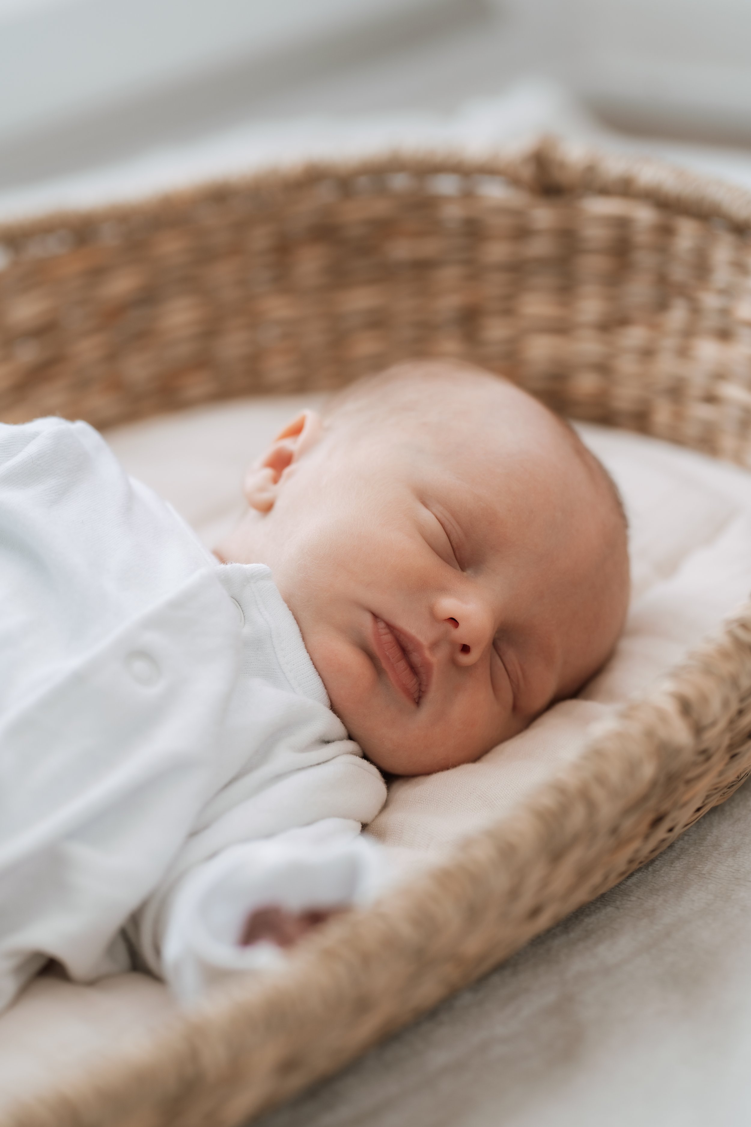A baby sleeping peacefully in a wicker basket, wearing a white outfit.