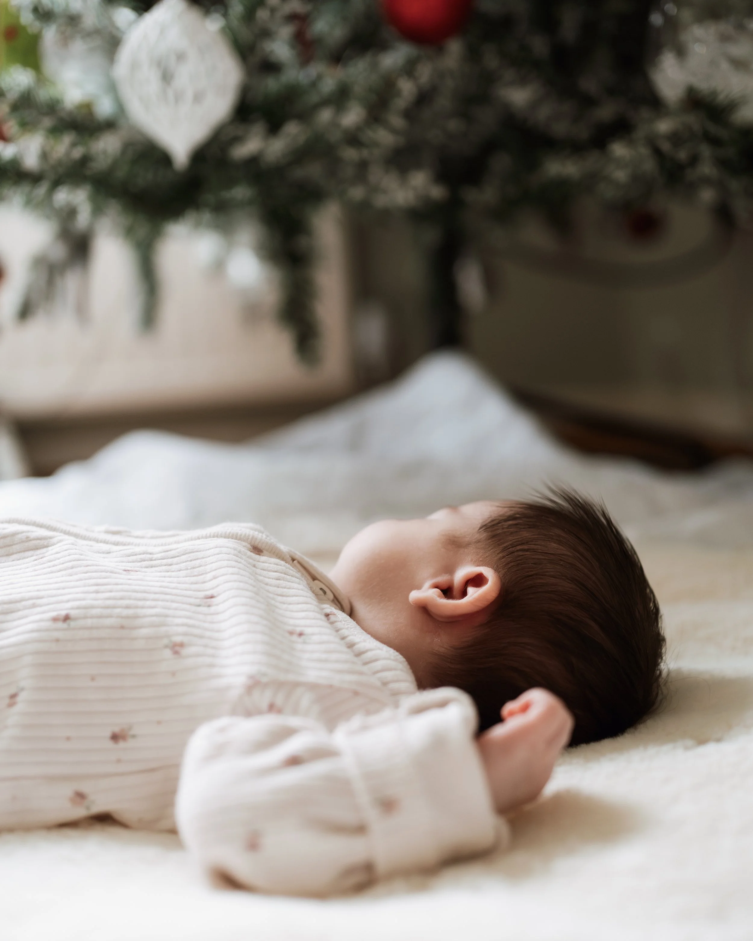 A baby sleeping on a bed with a Christmas tree in the background.