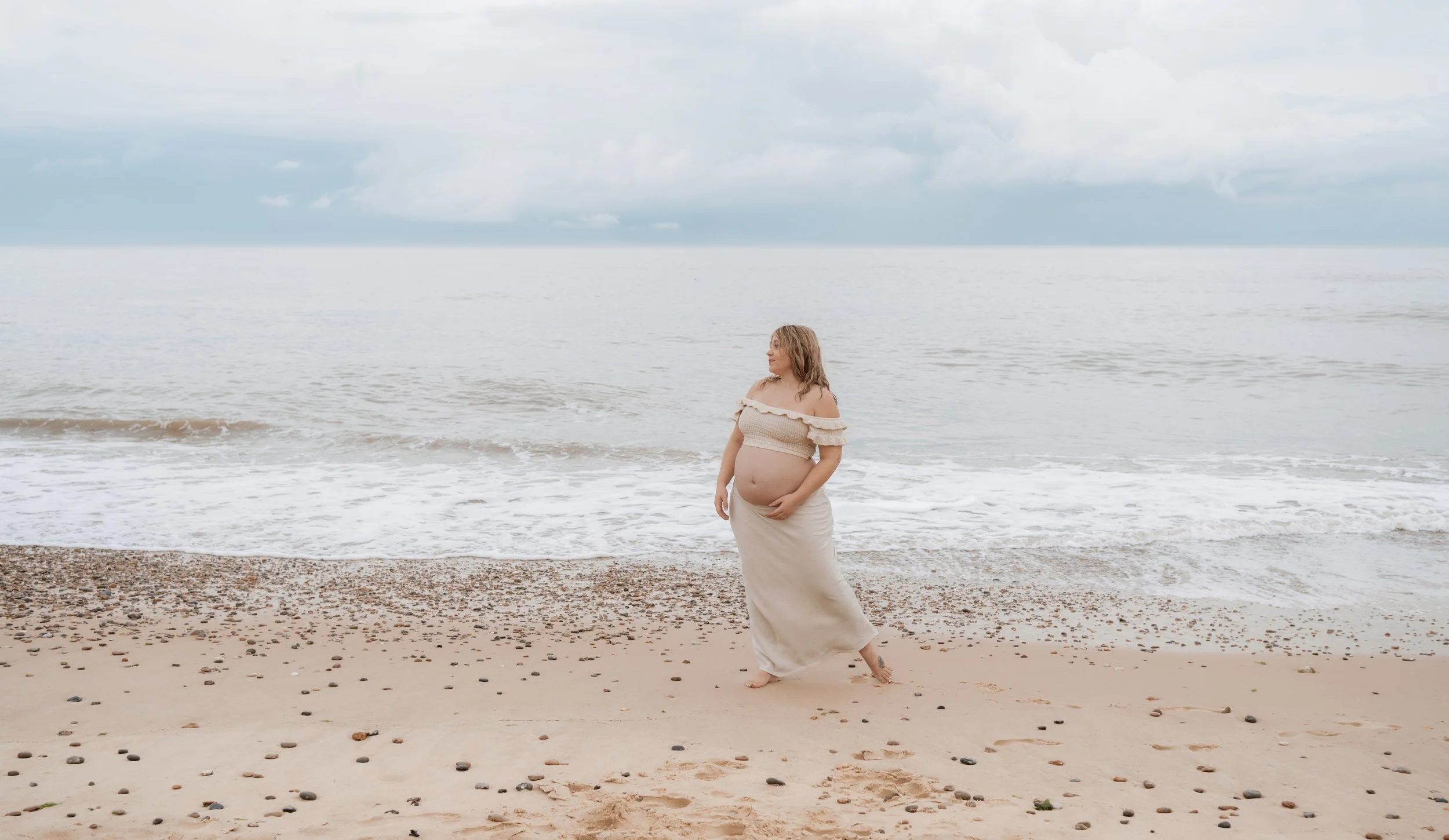 Pregnant woman standing on the beach with the ocean in the background