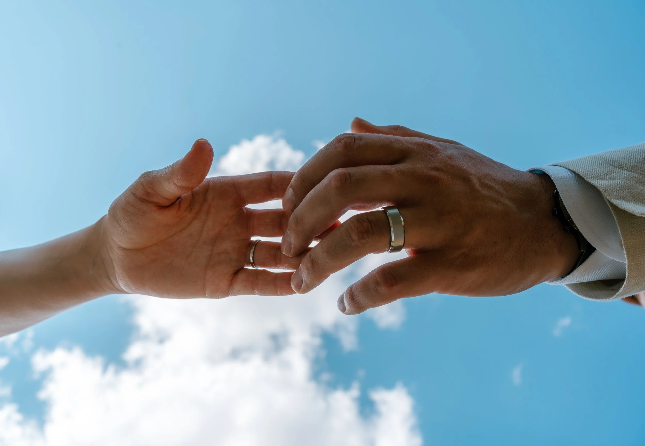 Newlyweds showing their wedding rings against a bright blue sky.