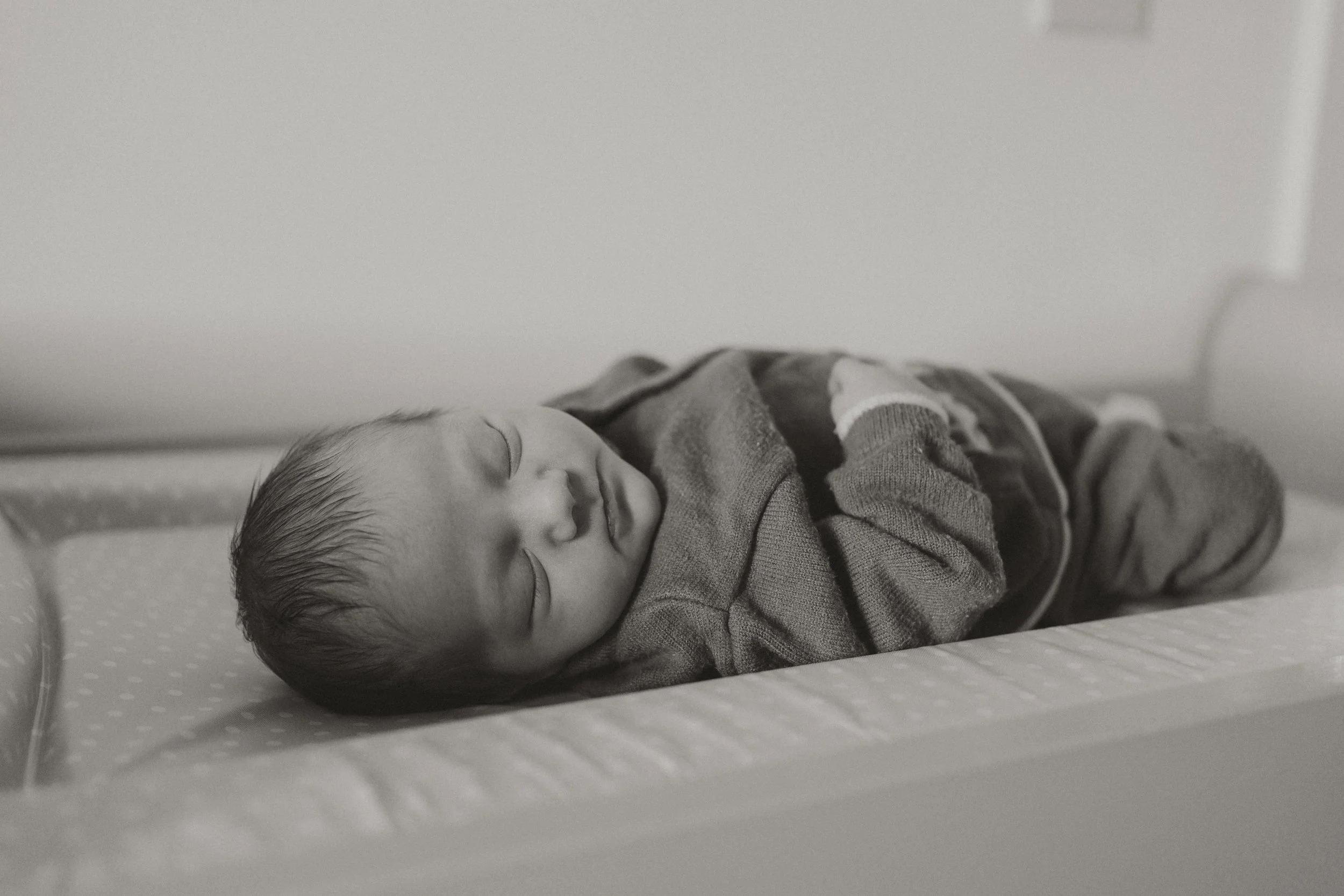 A baby sleeping peacefully on a mattress, dressed in a striped long sleeve shirt and pants, in a black and white photo.