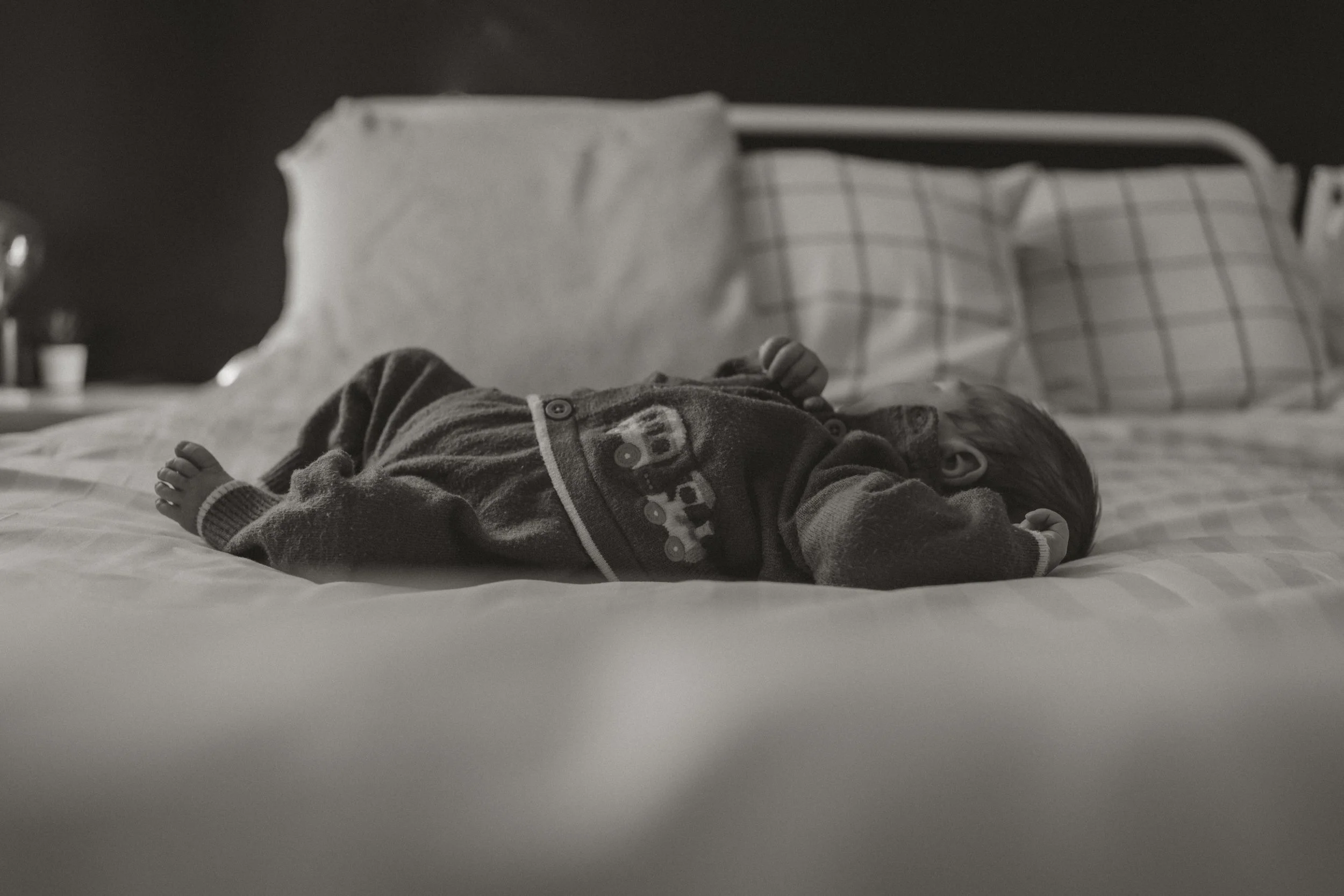 A young child lying on a bed with striped pillows, wearing a patterned sweater.