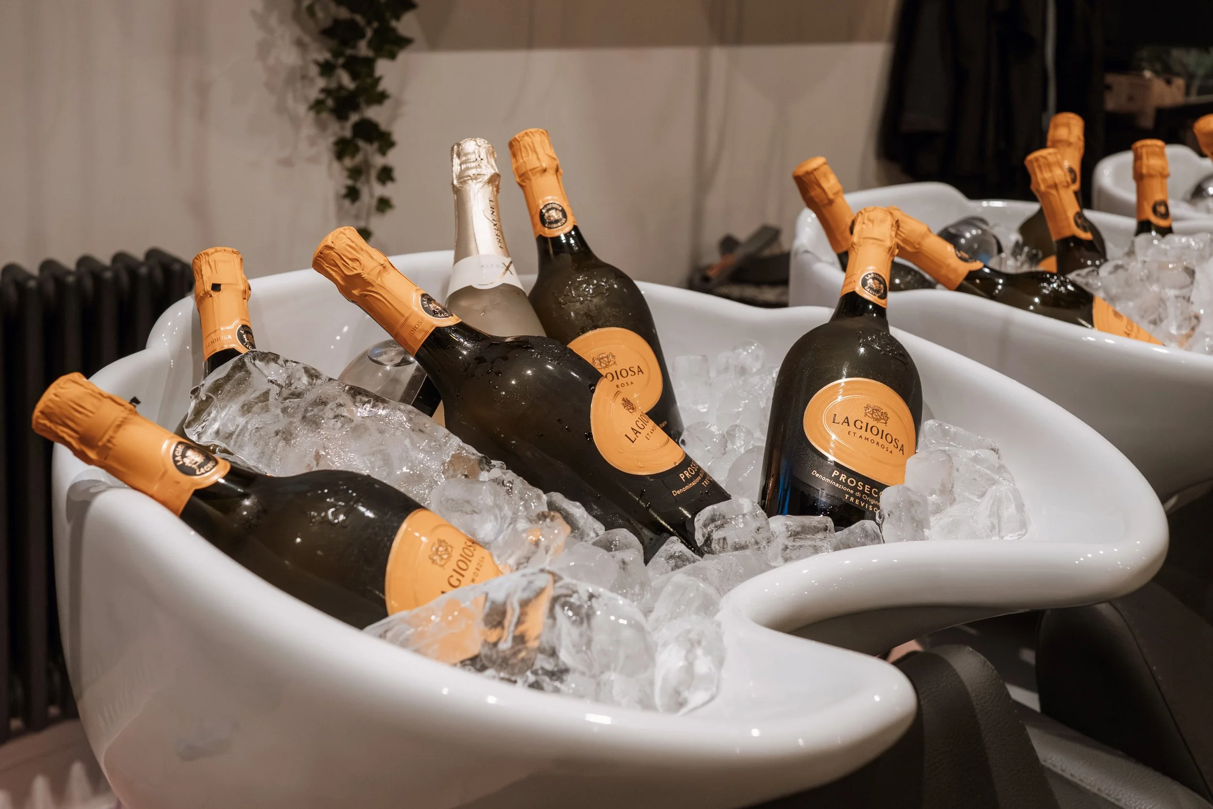 Bottles of La Gioiosa Prosecco in white ceramic tubs filled with ice at a party or event.