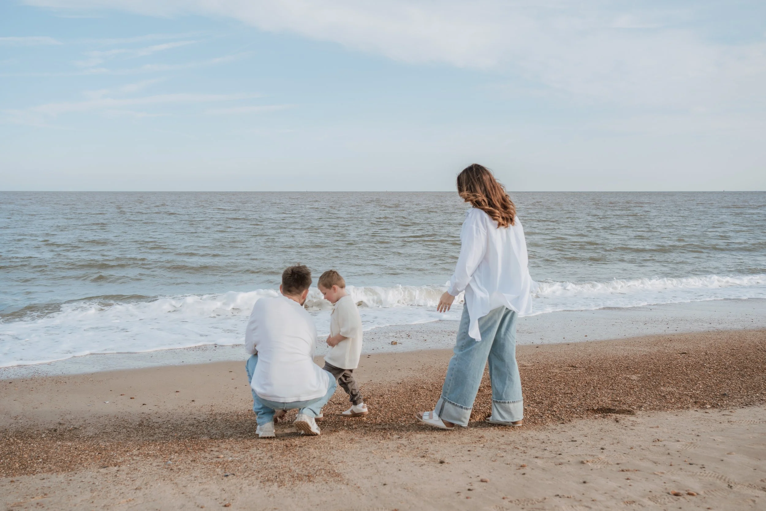 A family of four on the beach with two children and two adults, with ocean waves in the background and a partly cloudy sky.