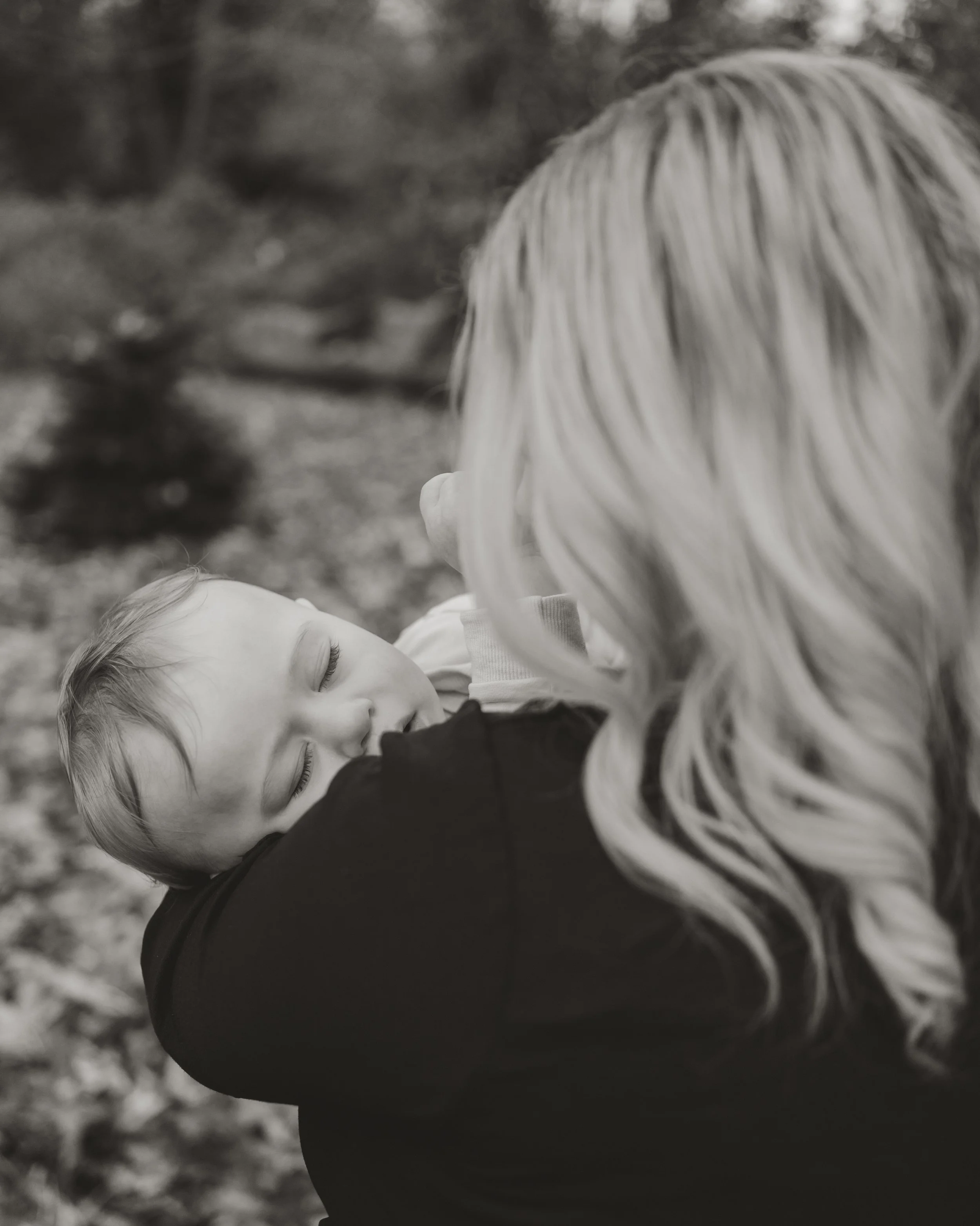 A young child asleep in a woman's arms outdoors in black and white.
