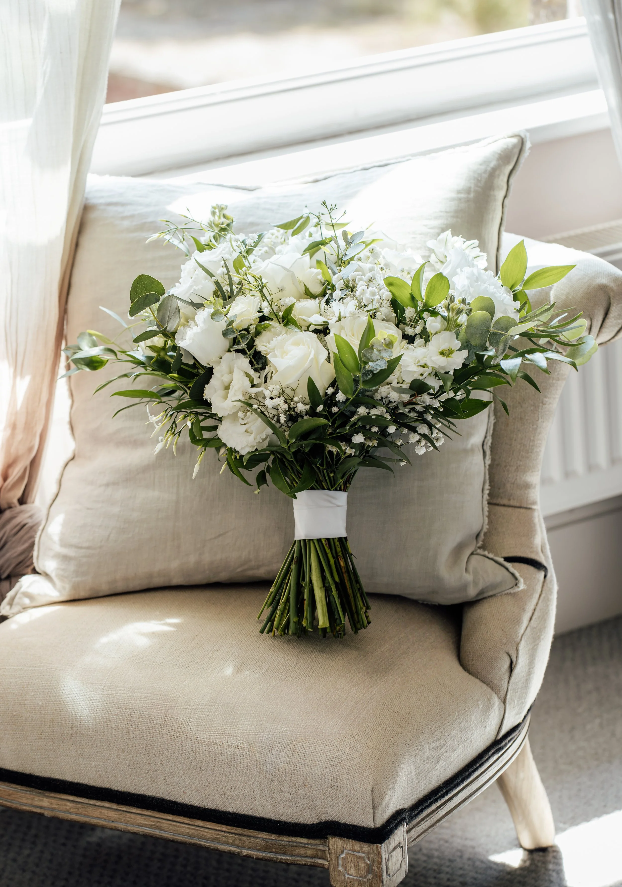 White and green wedding bouquet resting on a neutral armchair.