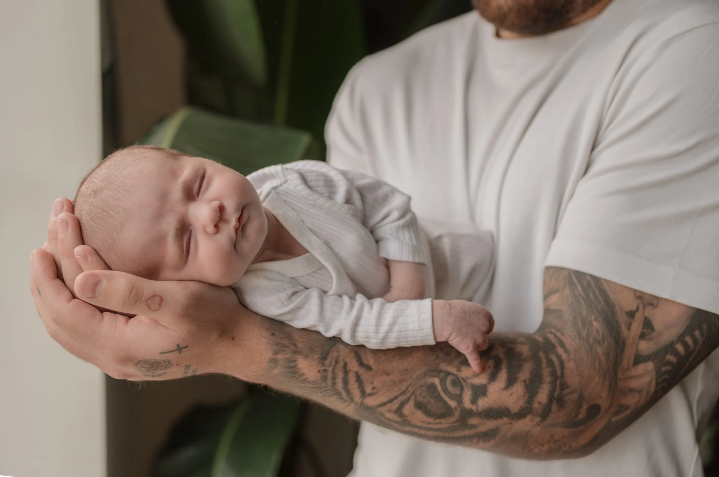 A man with tattoos on his arm holding a sleeping newborn baby in his hand.