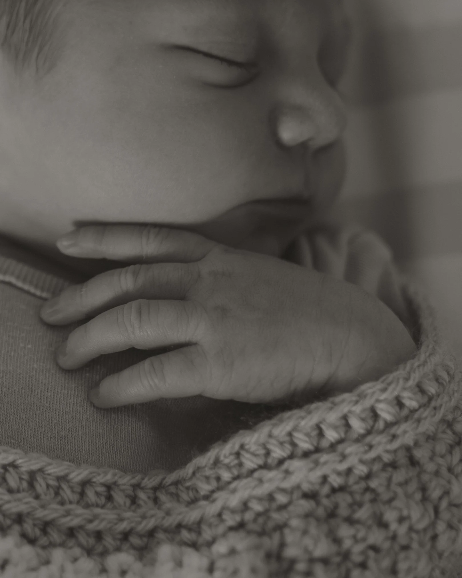 Close-up of a sleeping baby resting their head on their hand with eyes closed, wearing a knitted sweater.