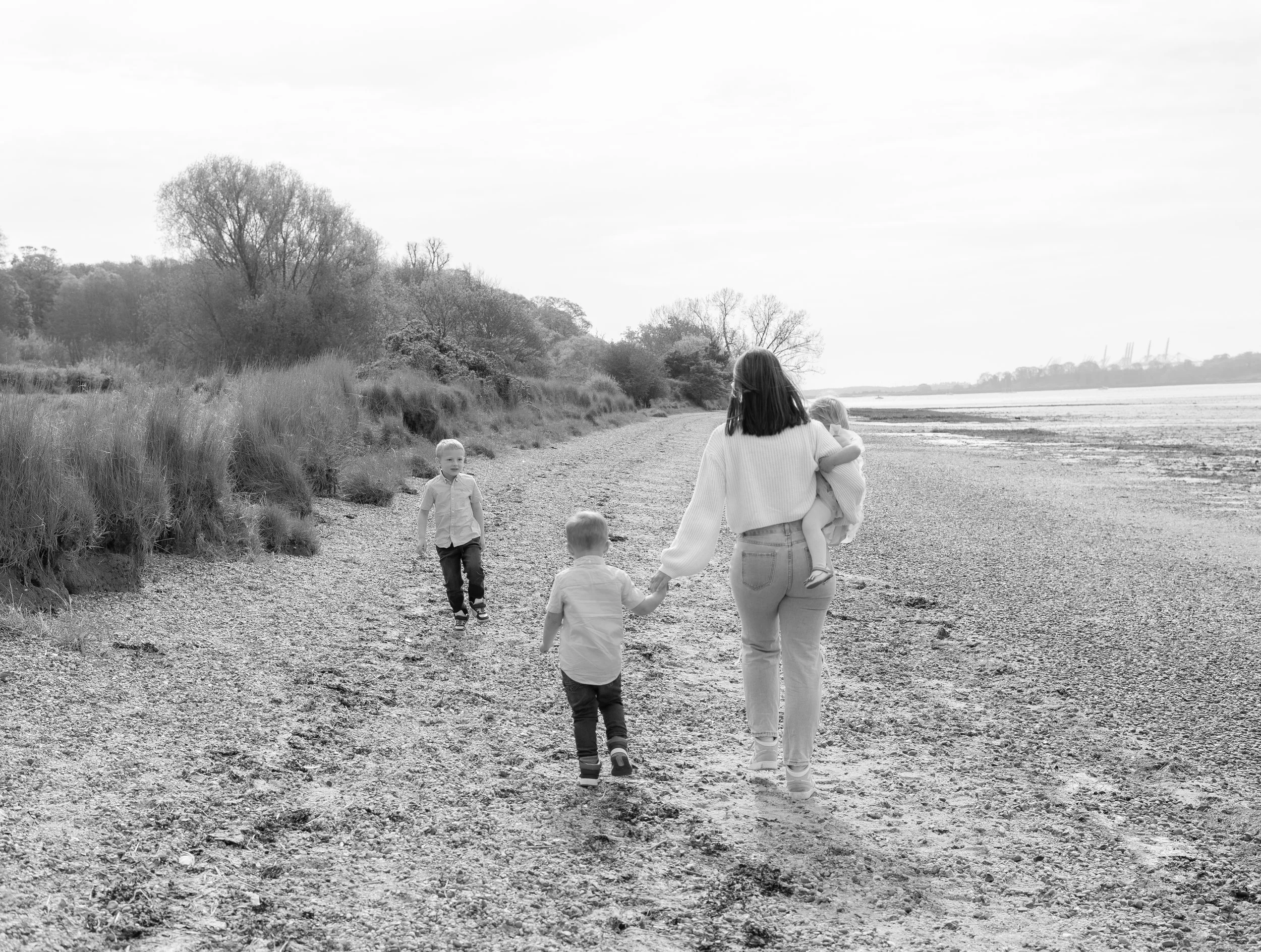Natural family photography at Nacton Shores in Suffolk, capturing a mother and her children walking along the shoreline, photographed by Gemma Wythe Photography.