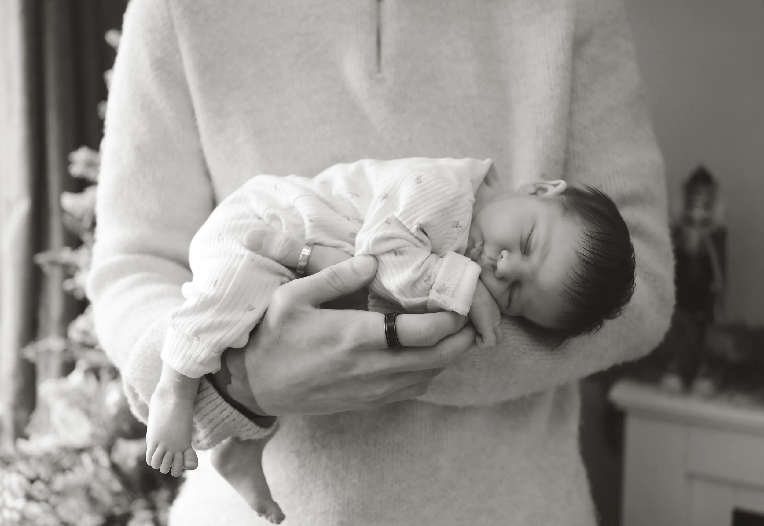 A person holding a sleeping baby in their arms. The baby is wearing pajamas and peacefully resting.