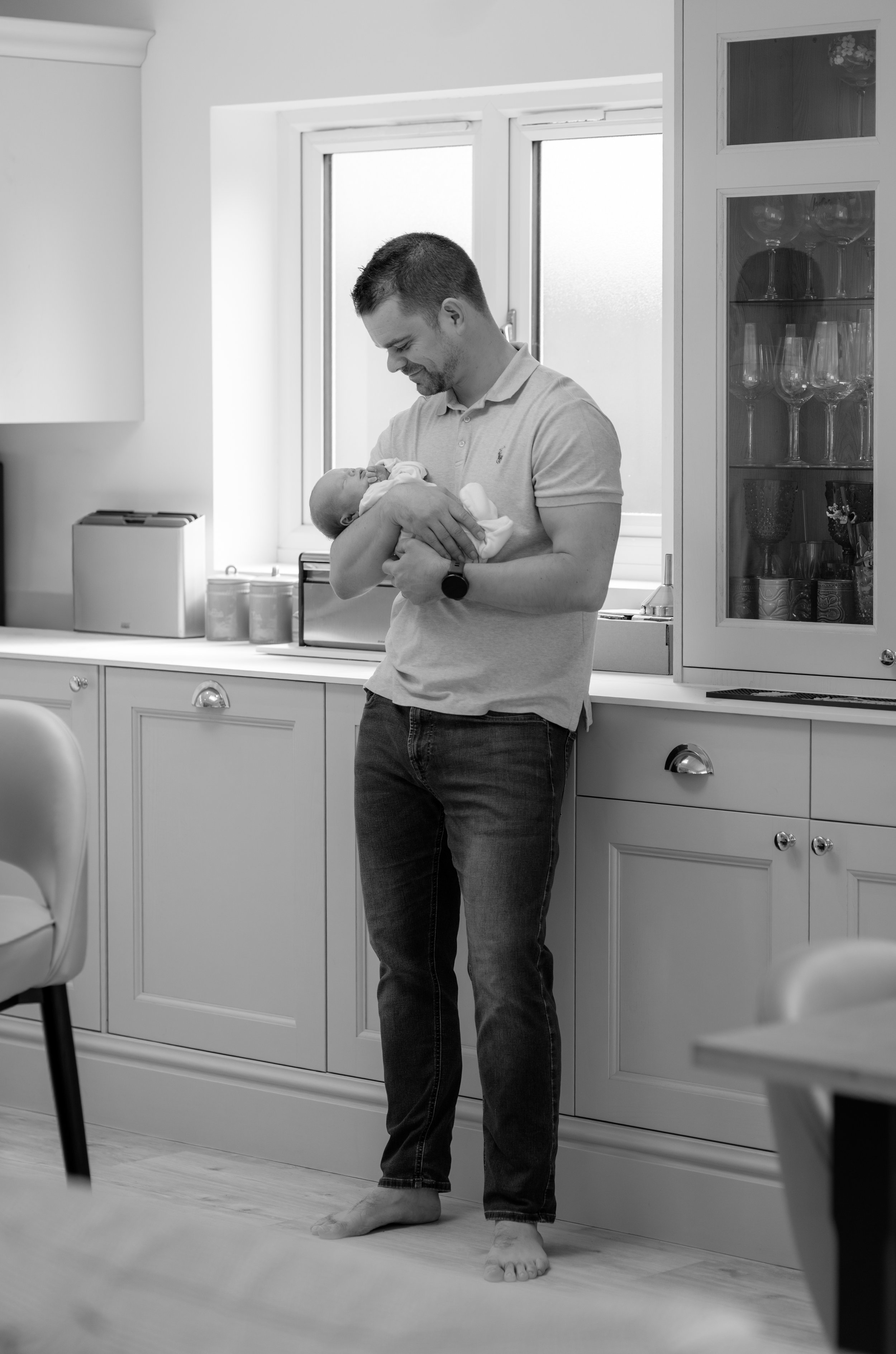 A man holding a newborn baby in a home kitchen.