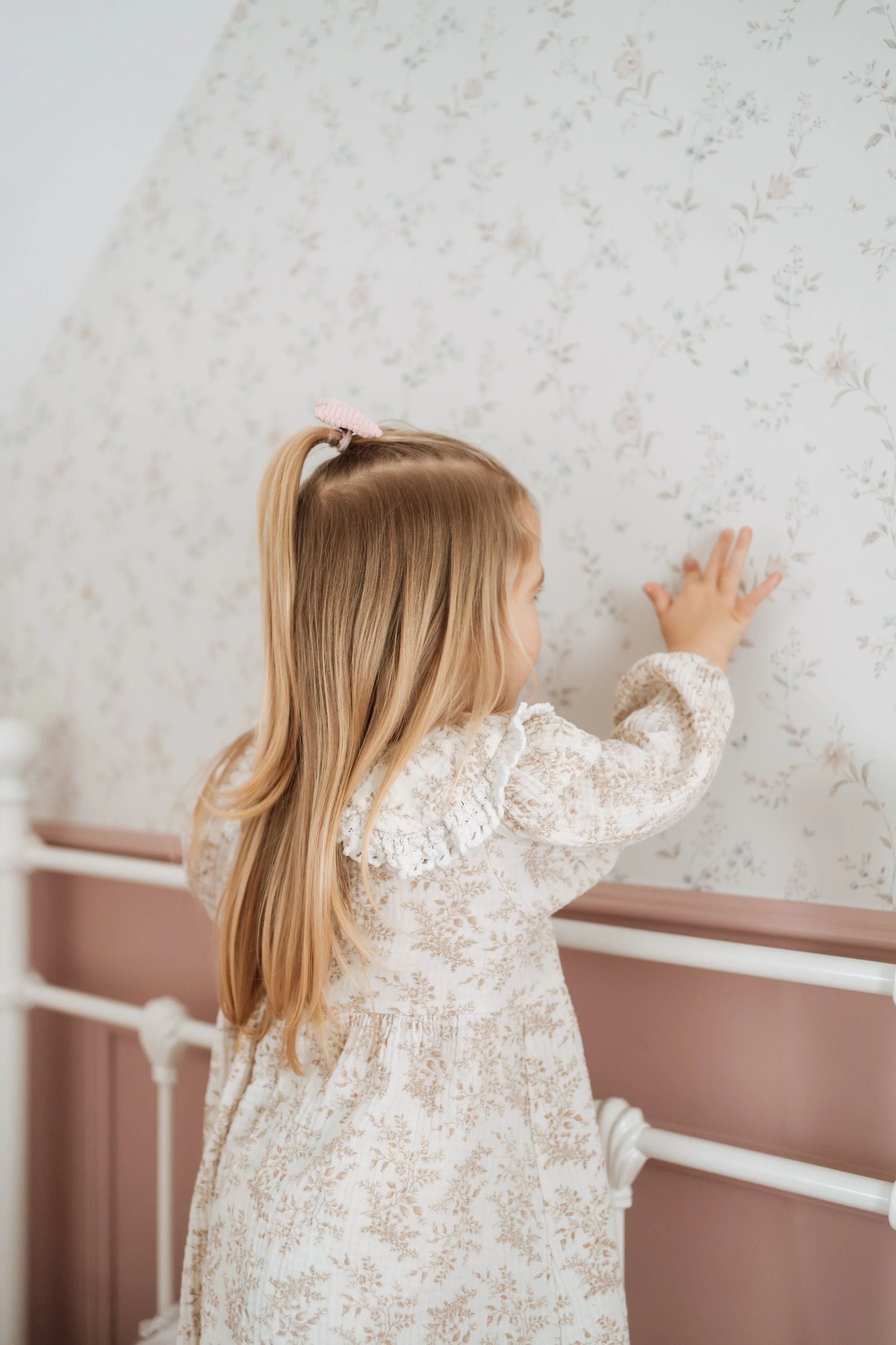 Child exploring a vintage nursery with soft pink panelling