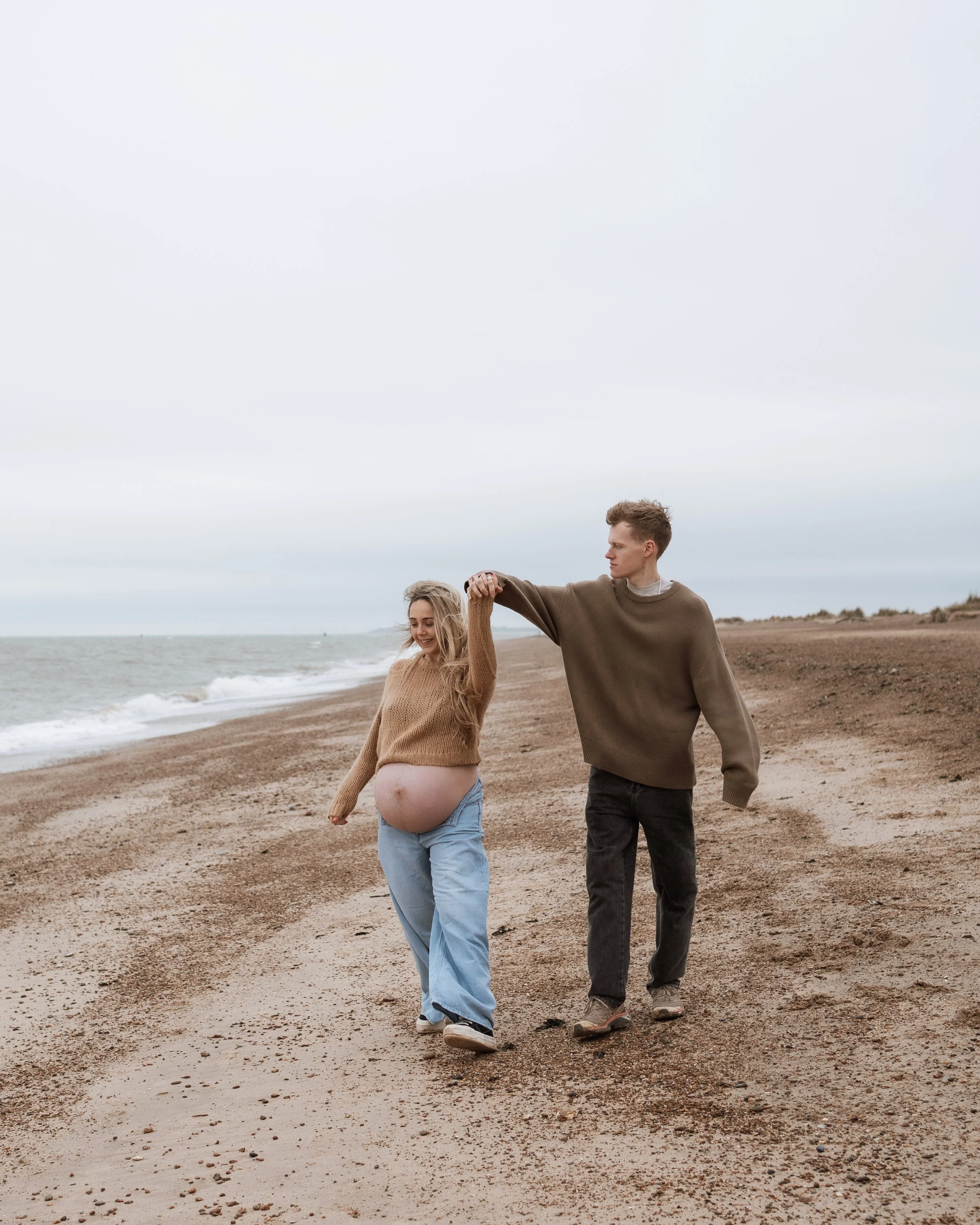 Pregnant woman and man holding hands walking on a beach