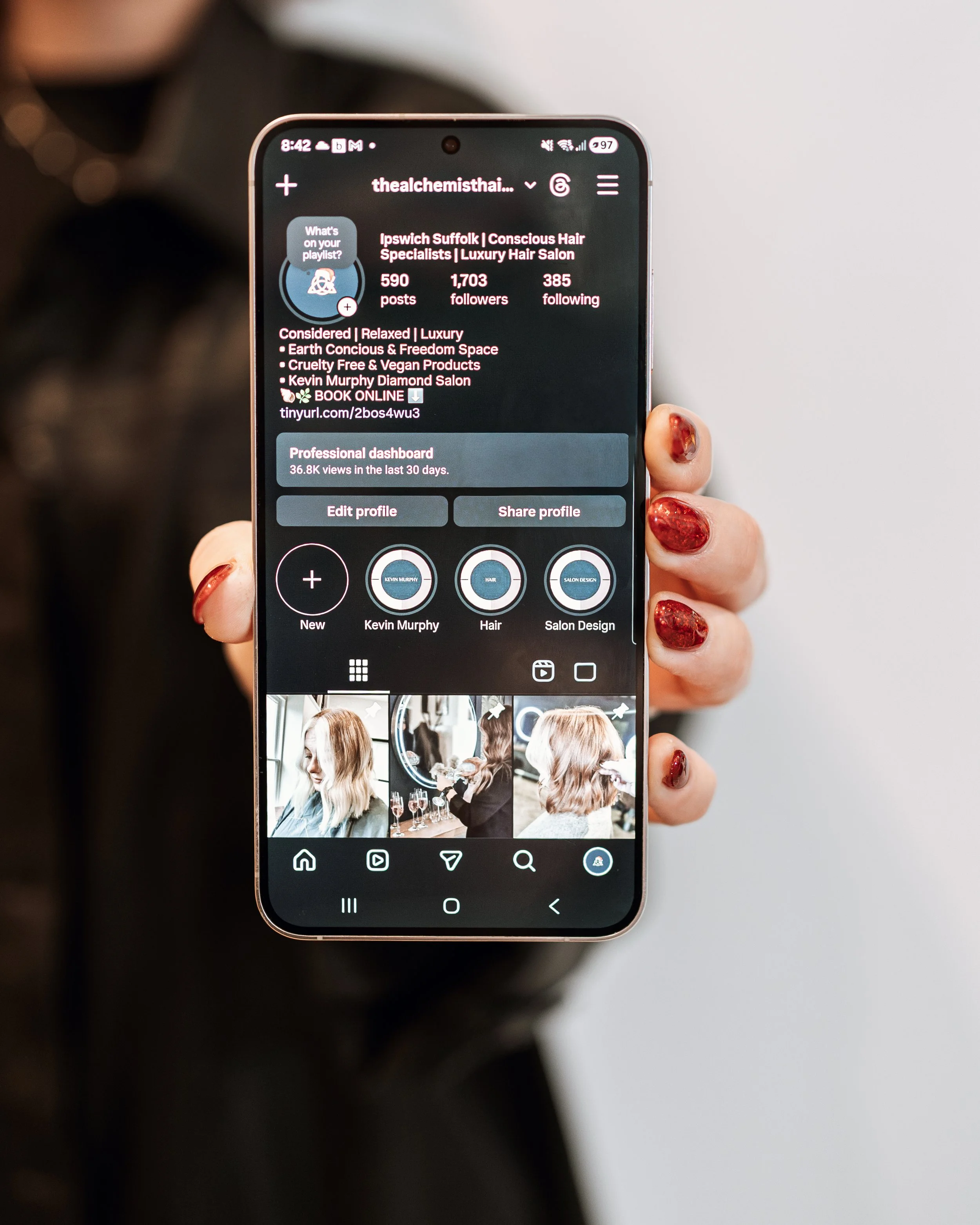 Person holding a smartphone displaying an Instagram profile of a hair salon with photos of women and interior shots.