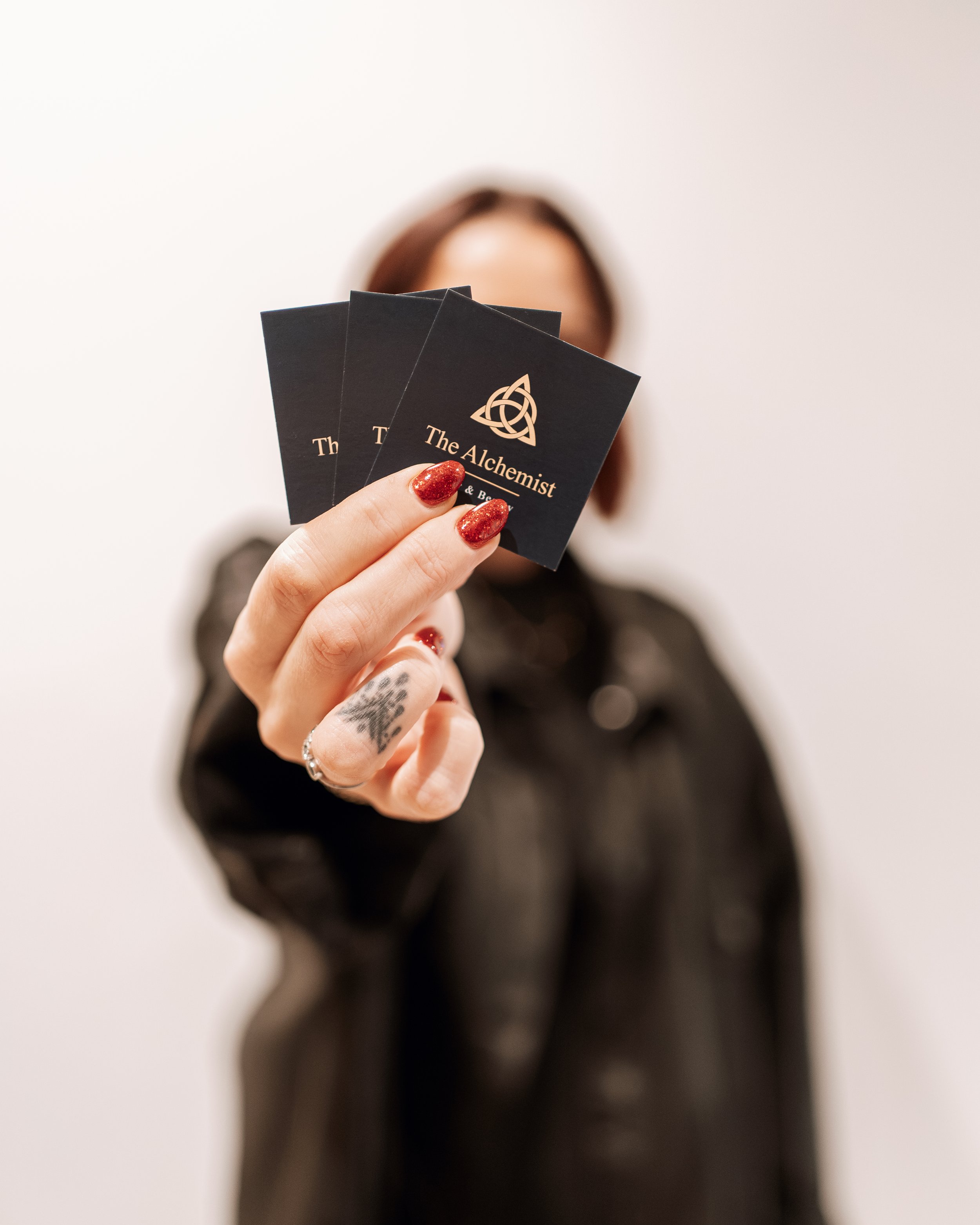 Person holding three black business cards with a gold alchemy symbol and the text "The Alchemist".
