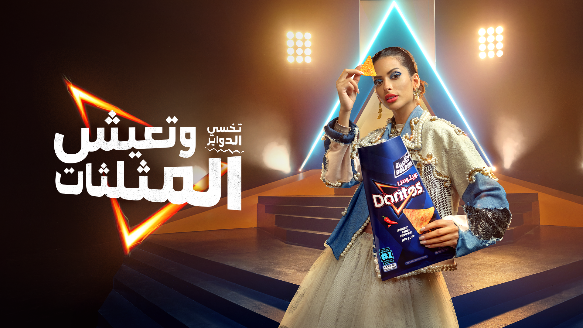 A woman in a fashionable outfit holding a bag of Doritos chips and an individual chip, standing on a stage with neon lights and stairs, with Arabic text promoting Doritos.