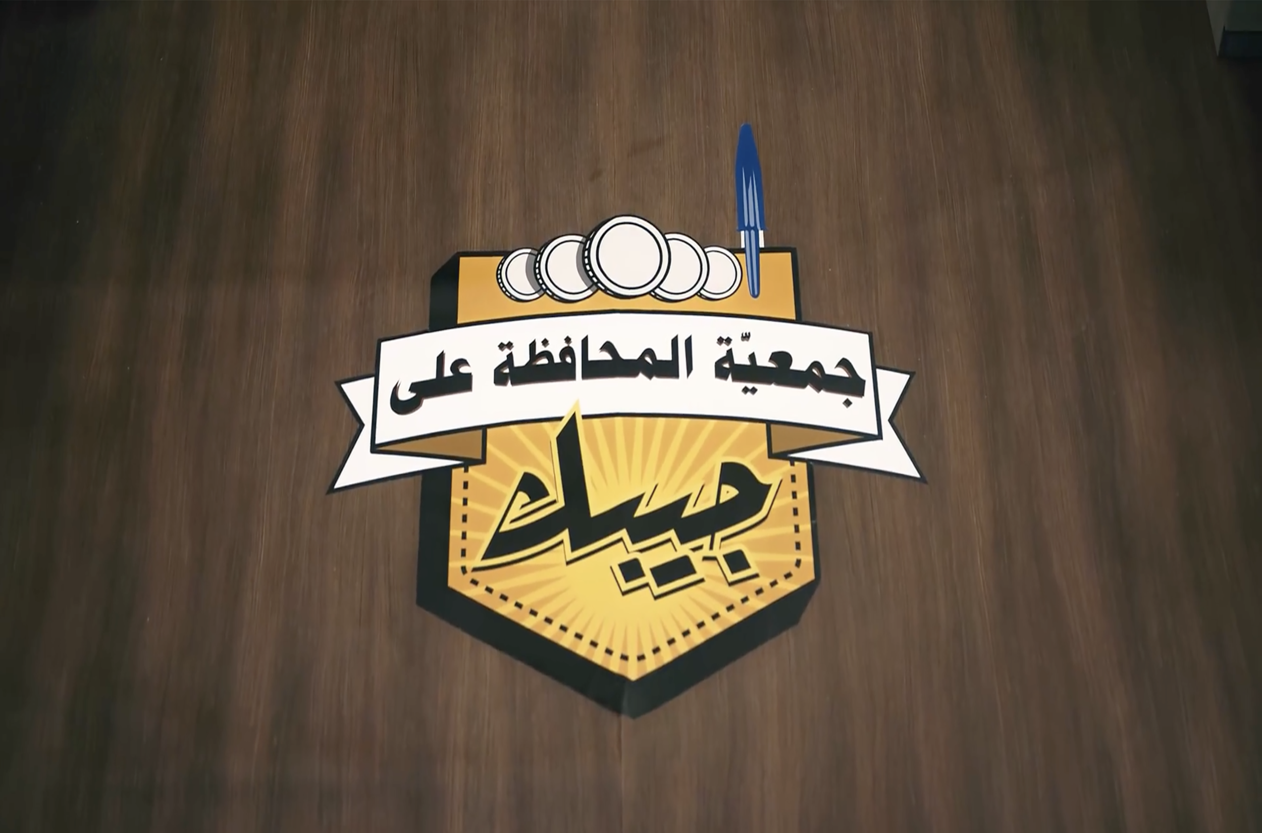 Logo of a local football club in Arabic with a badge design, coins, and a pen.