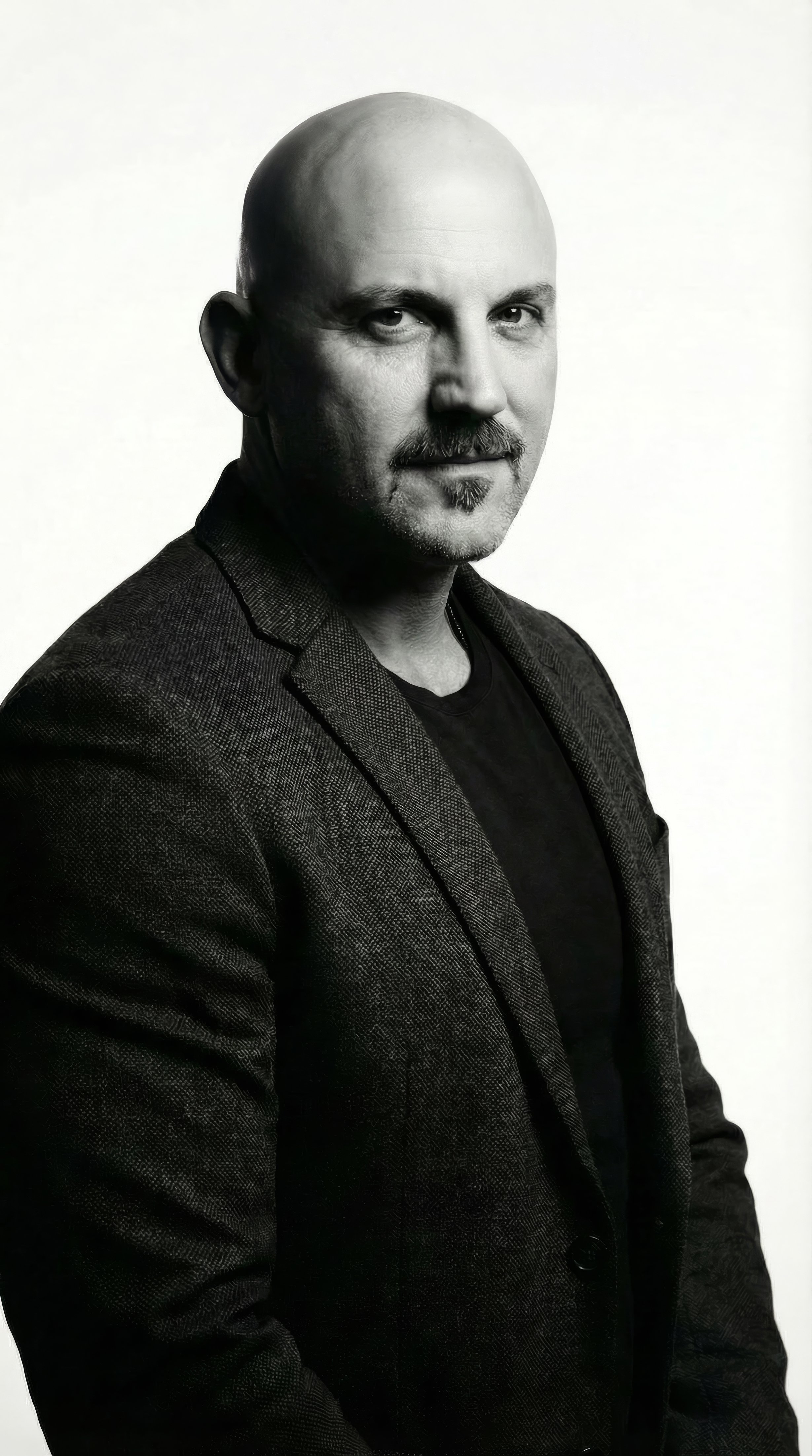 Black and white portrait of a man with a beard and mustache, wearing a dark blazer over a t-shirt, looking at the camera.